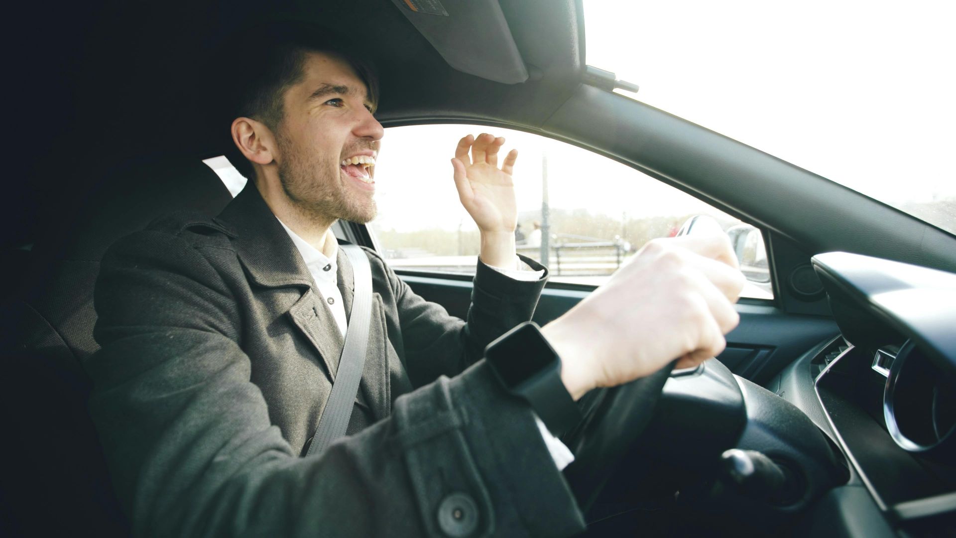Cheerful man driving and singing inside a car, enjoying a sunny day.