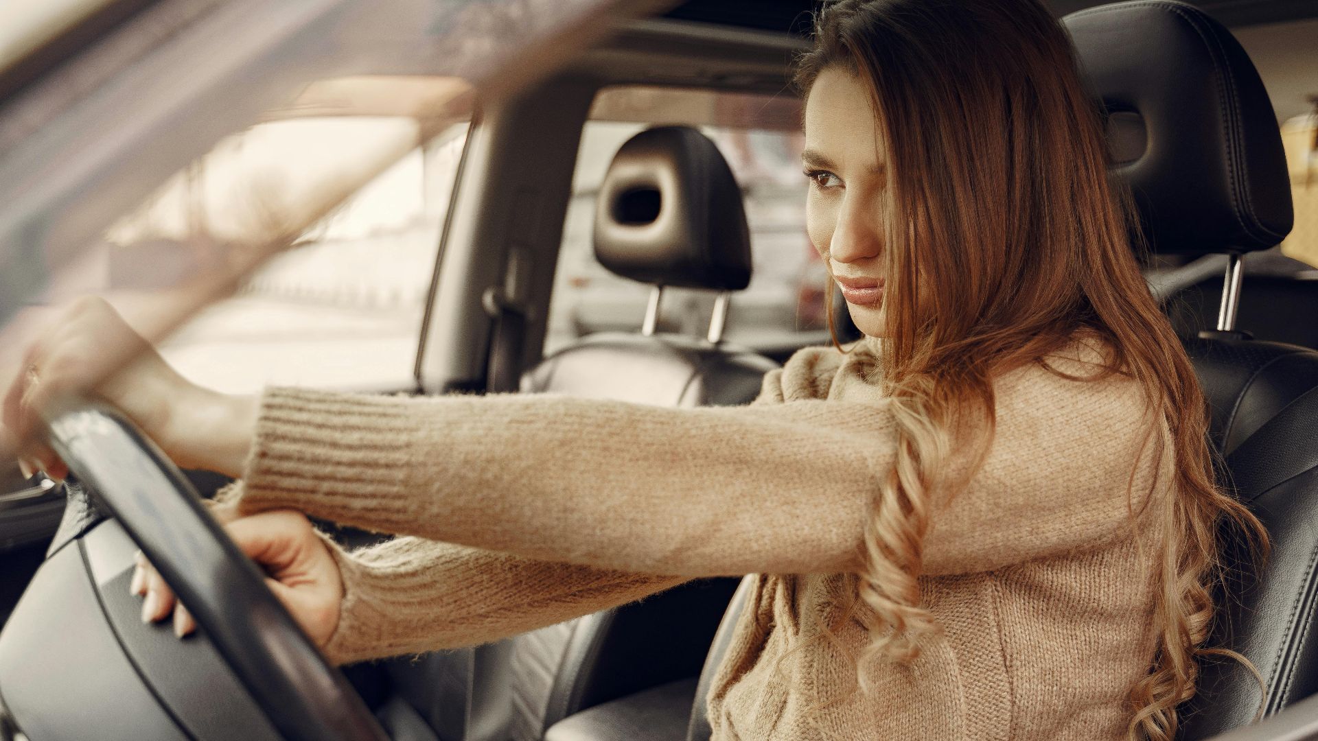 Side view of concentrated contemporary female driver in casual clothes going along street road alone by car with leather interior