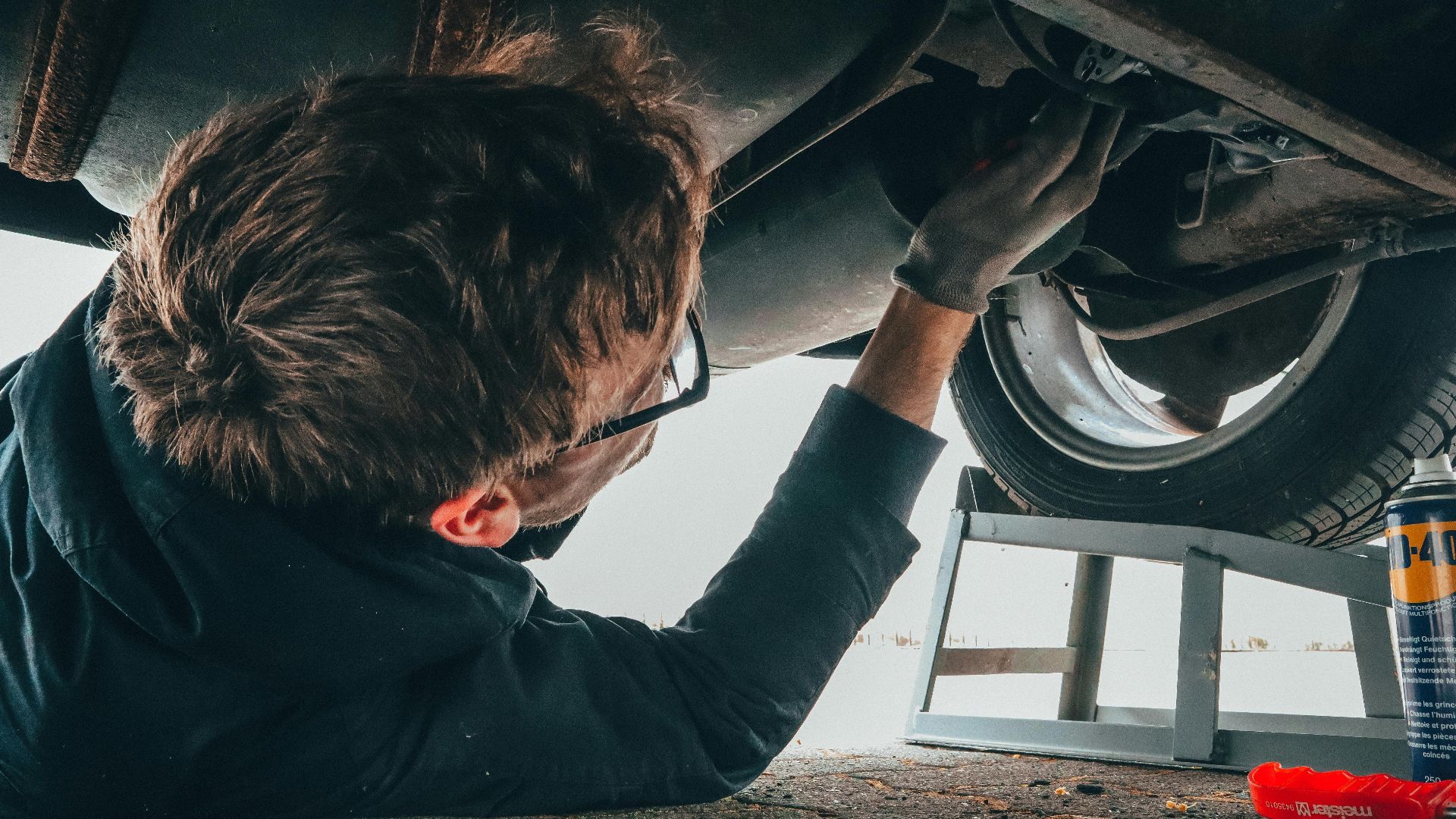 Mechanic skillfully repairing car undercarriage in outdoor setting with tools.