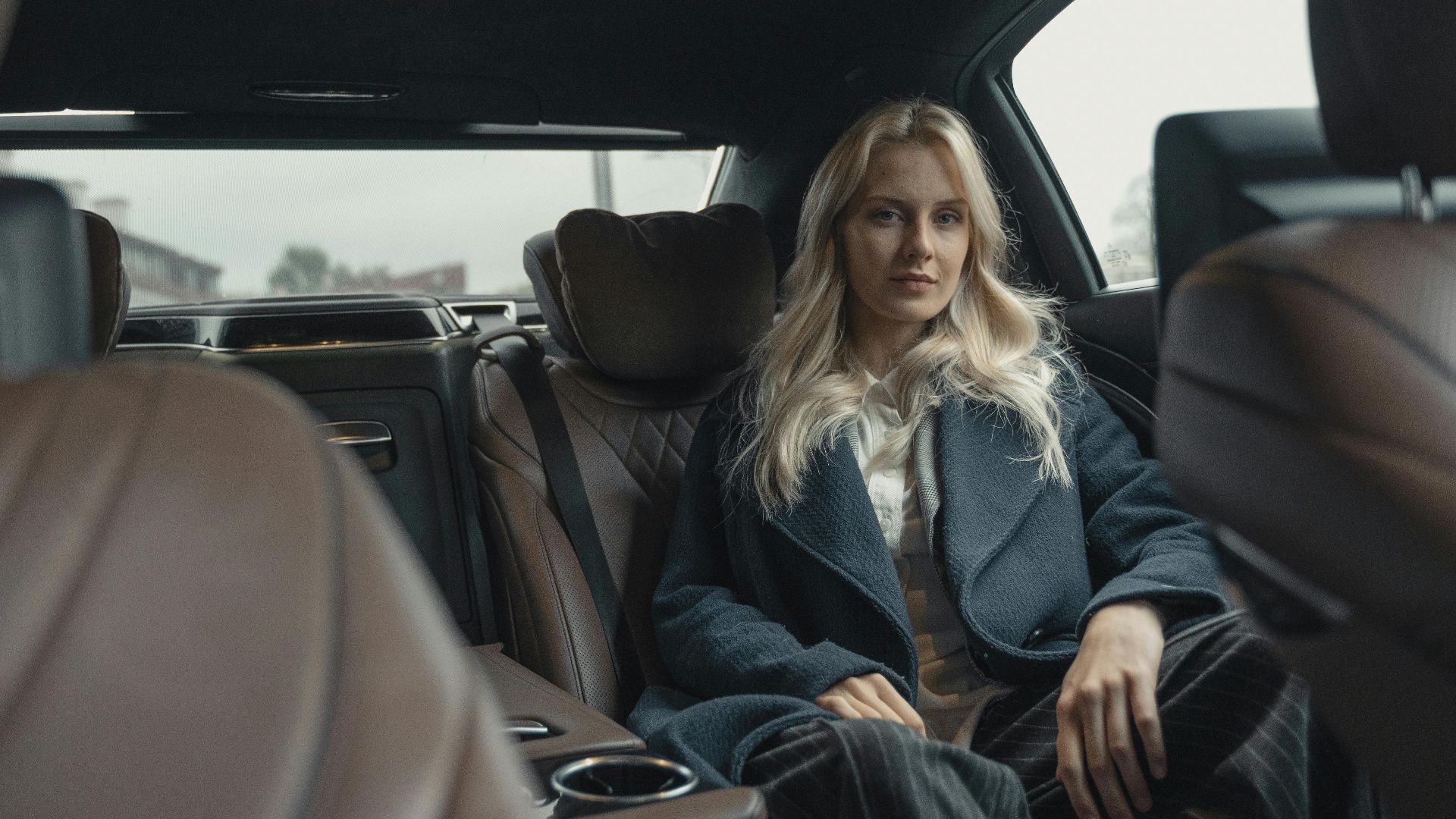 Elegant woman in a blue coat sitting in the back seat of a luxury car.