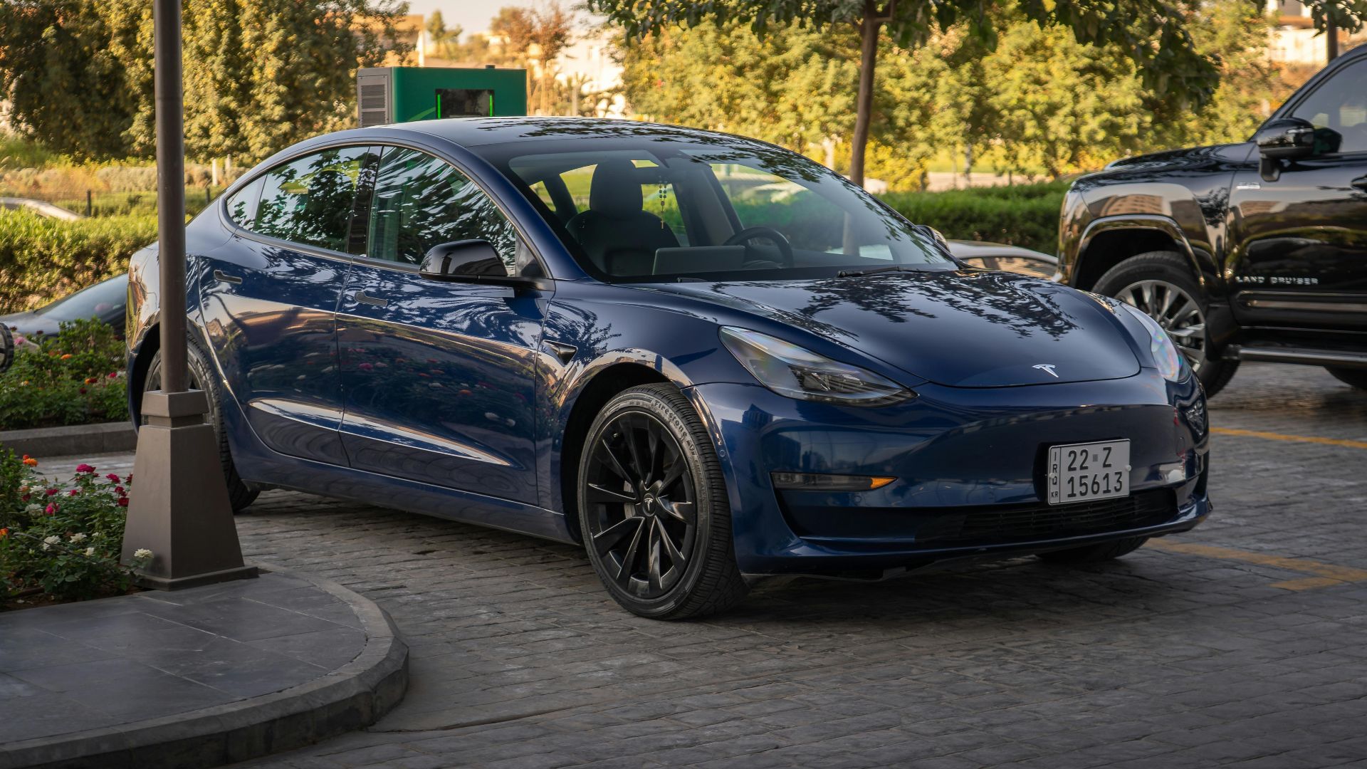 Electric blue Tesla Model 3 parked in sunlit commercial parking area.