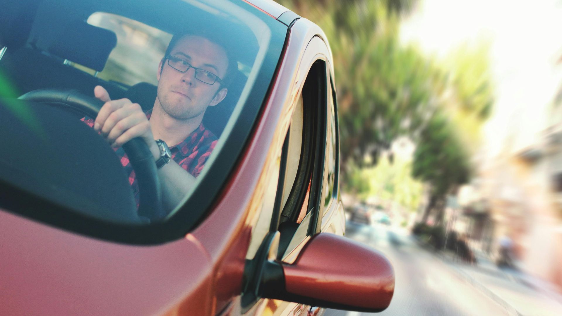 A man driving fast through a city street in a red car, showcasing motion and focus.