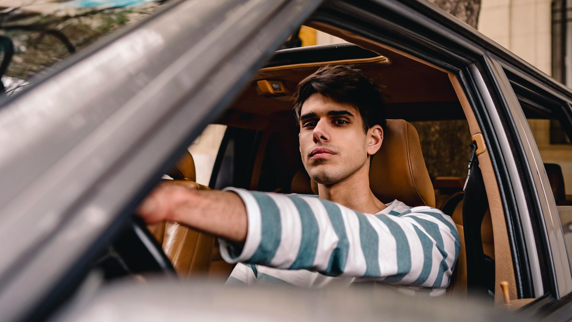 A young man with short brown hair confidently driving a car, seen through the window.