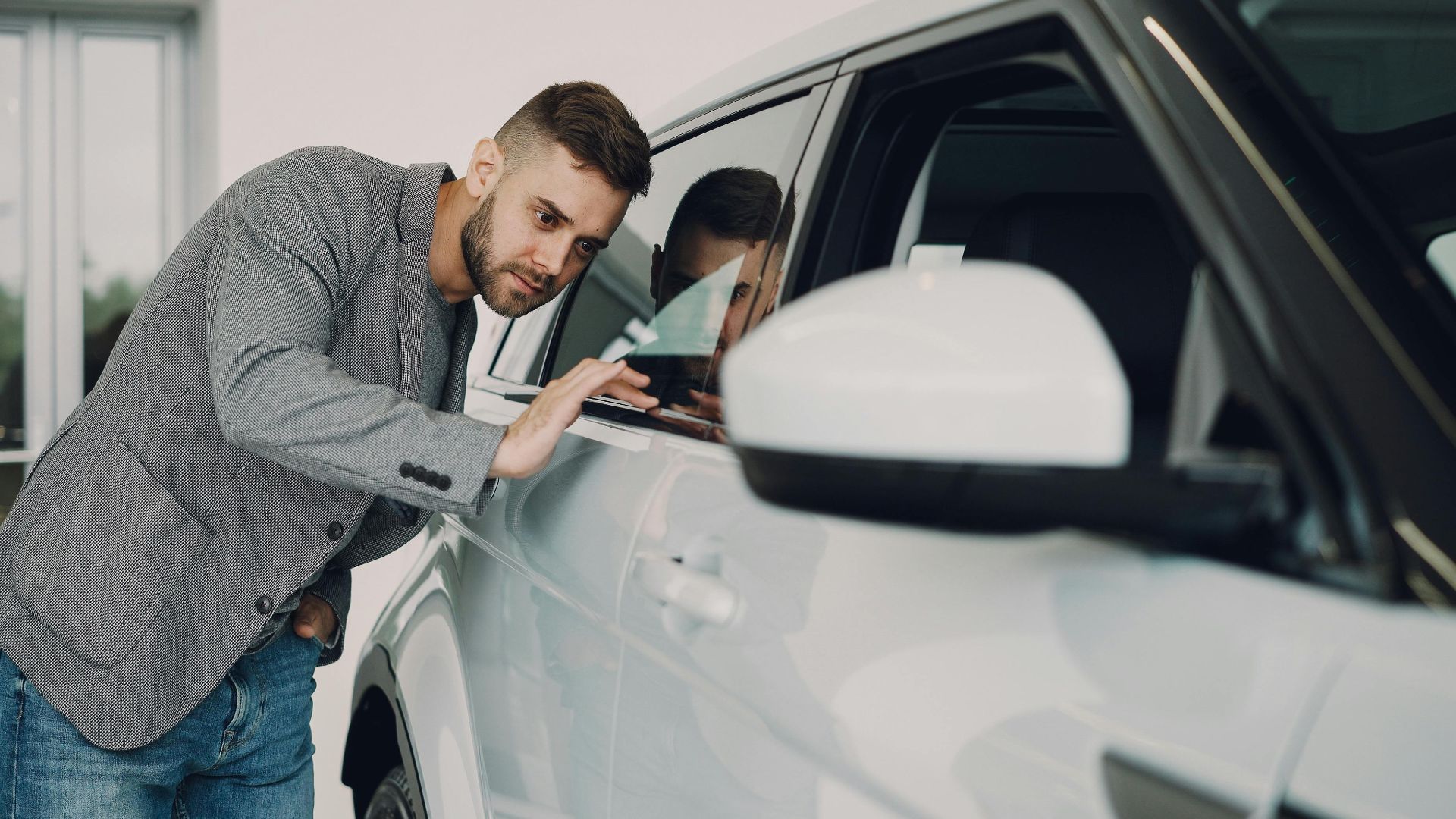 Man carefully examining a modern white car at a dealership showroom.