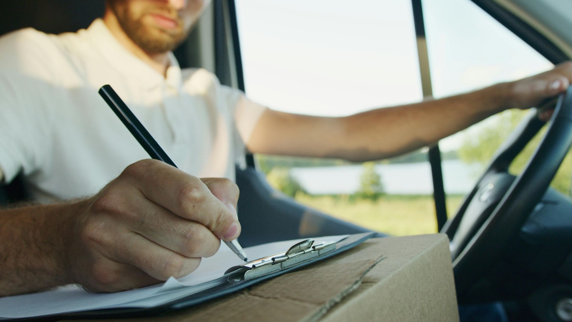 Close-up of a delivery driver inside a van writing on a clipboard. Logistics and service work concept.