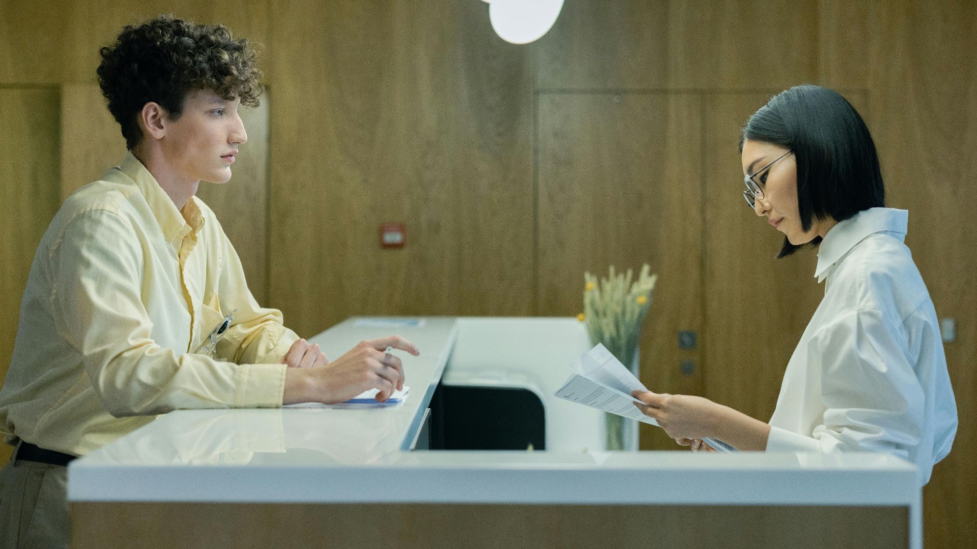 A young man and woman interacting at a modern office reception desk indoors.