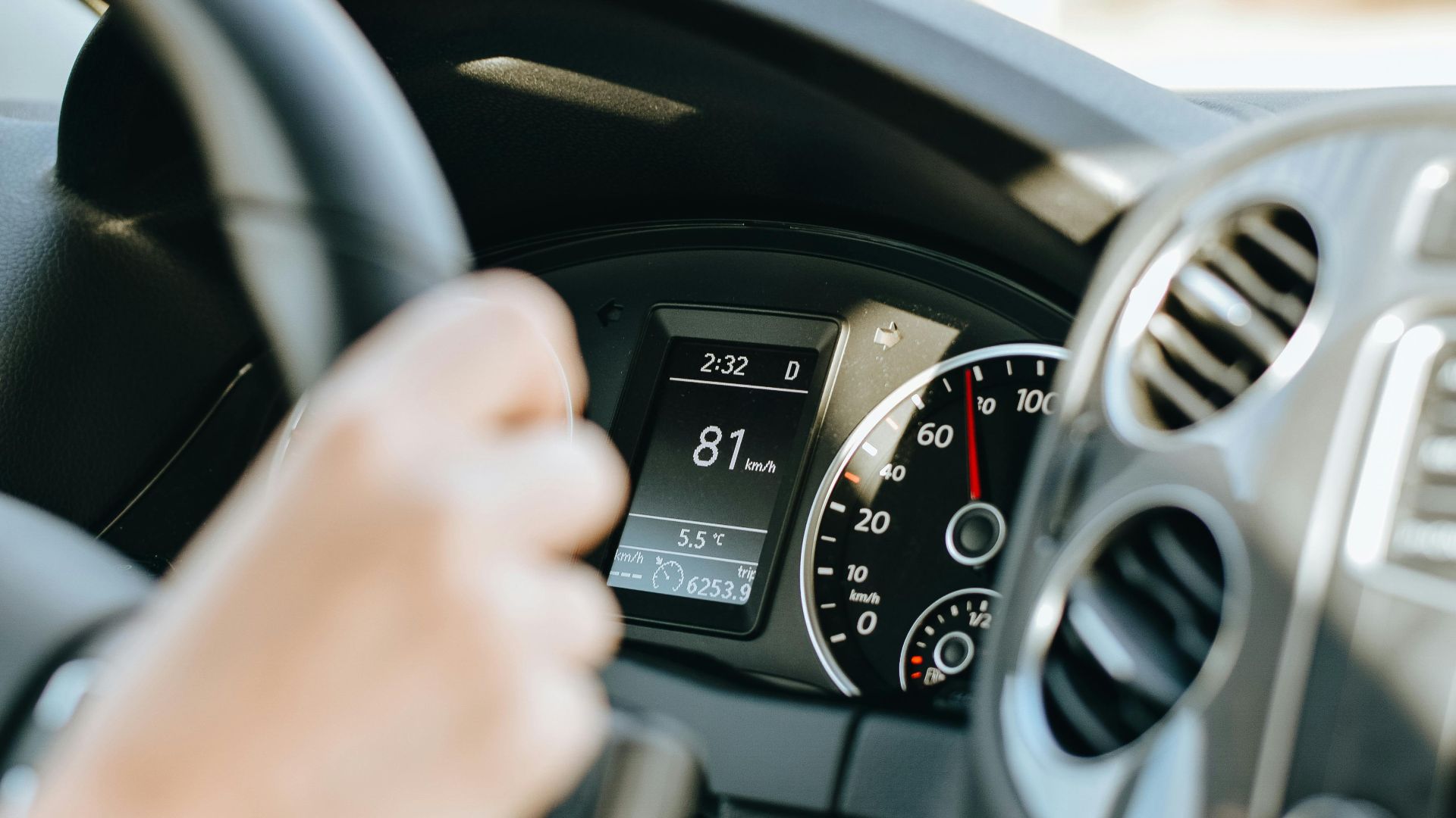 Crop anonymous person holding black steering wheel and driving car in sunny day