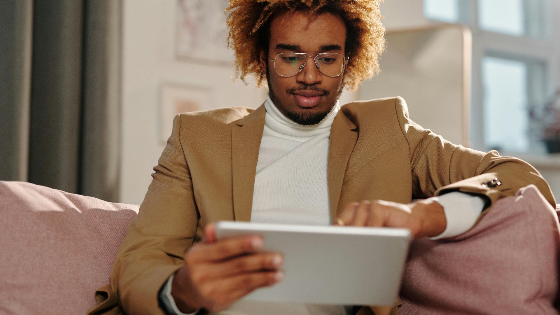Stylish young man with curly hair using a tablet while relaxing indoors.