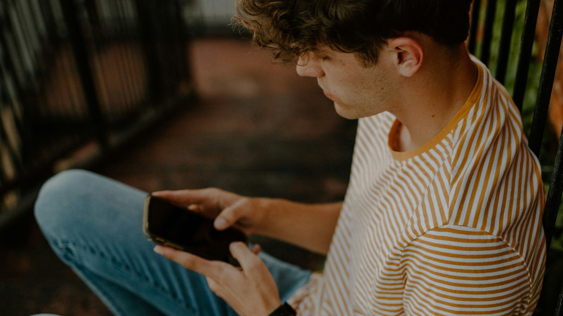 man in white and brown stripe shirt and blue denim jeans sitting on brown wooden bench