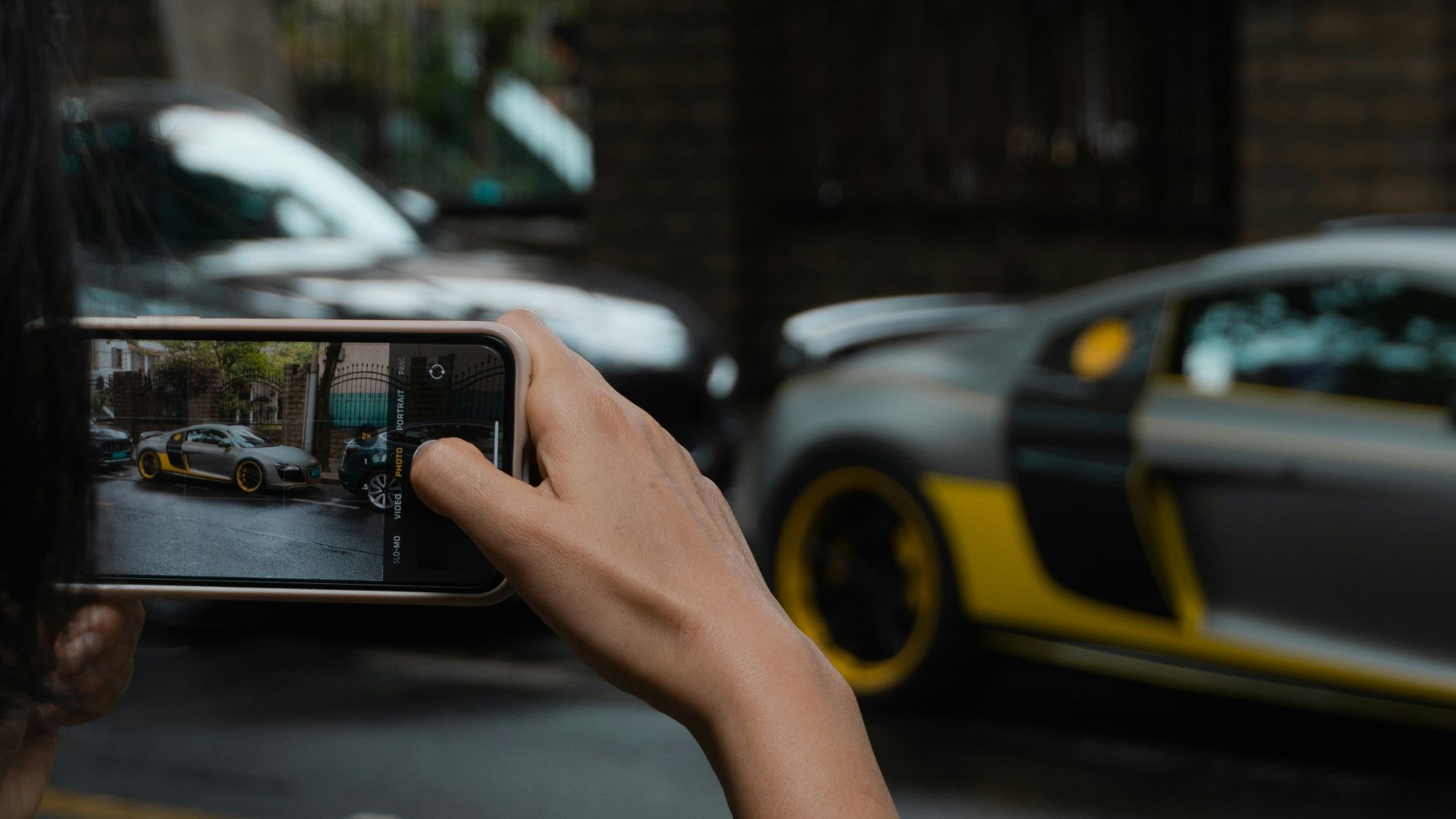 person holding black smartphone taking photo of cars on road during daytime