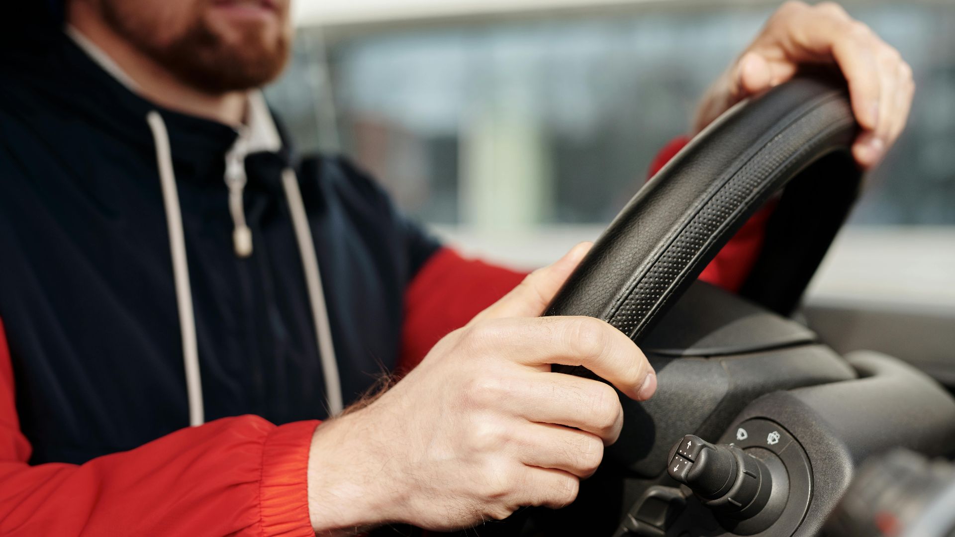 Focused man holding steering wheel, driving in vehicle interior. Close-up view with selective depth.