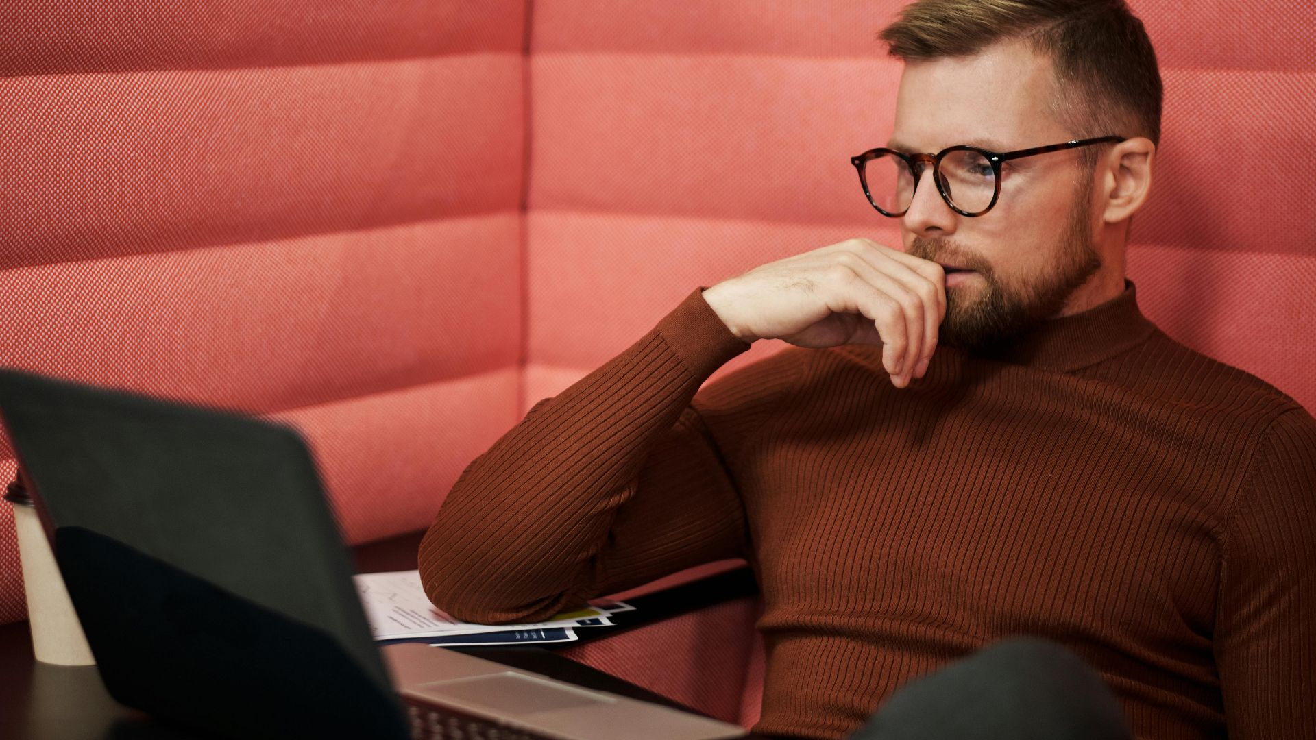 Concentrated businessman wearing eyeglasses working on a laptop indoors.