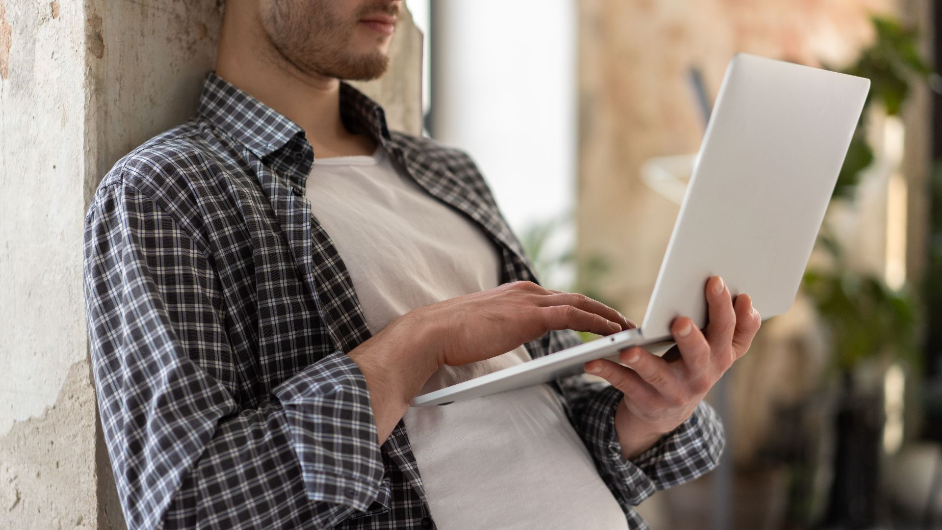 Casual young man in plaid shirt using laptop indoors. Modern lifestyle and technology.