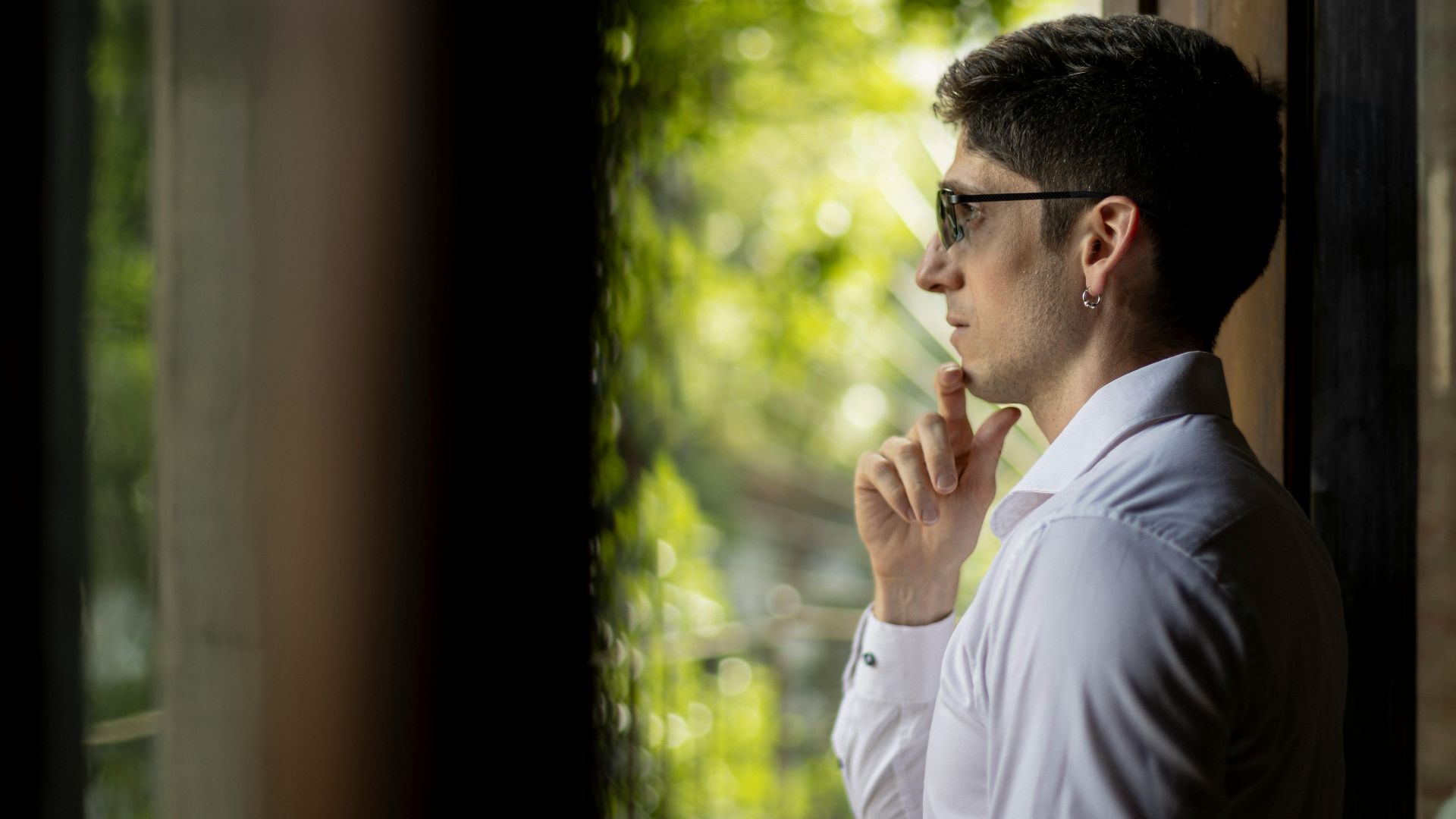 Young man in white shirt peers thoughtfully out a window in Buenos Aires.