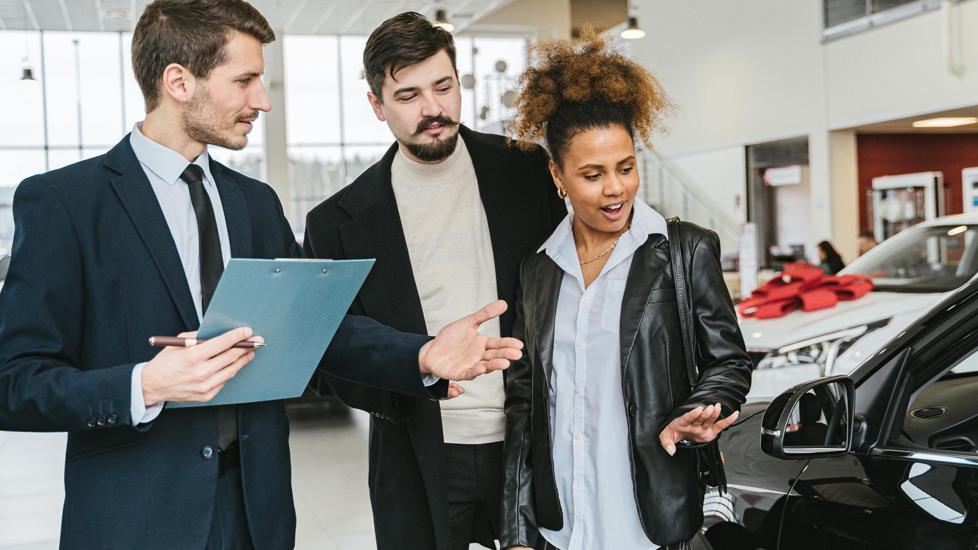 A diverse group of adults discussing vehicles at a bright modern car dealership.