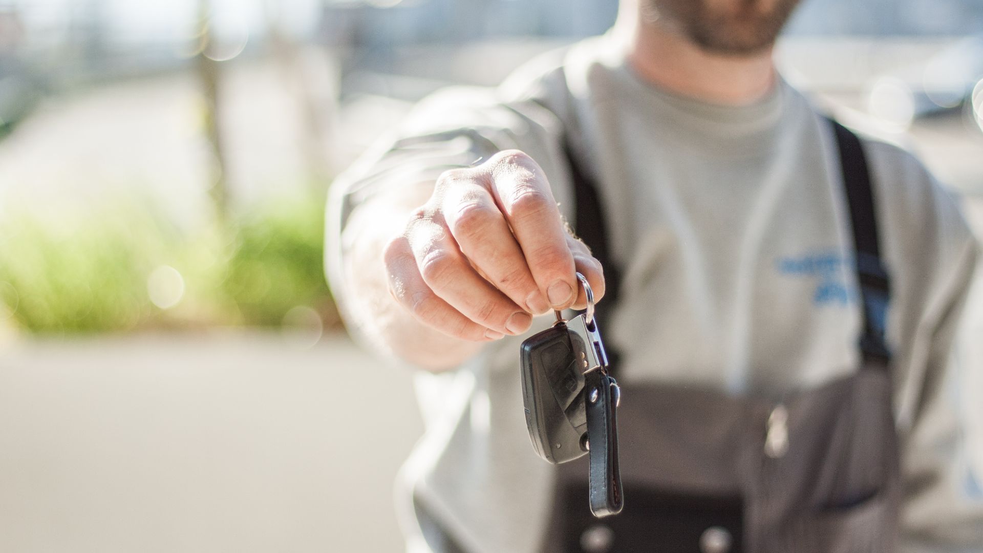 Hand holding a car key outdoors, blurred background, shallow focus.