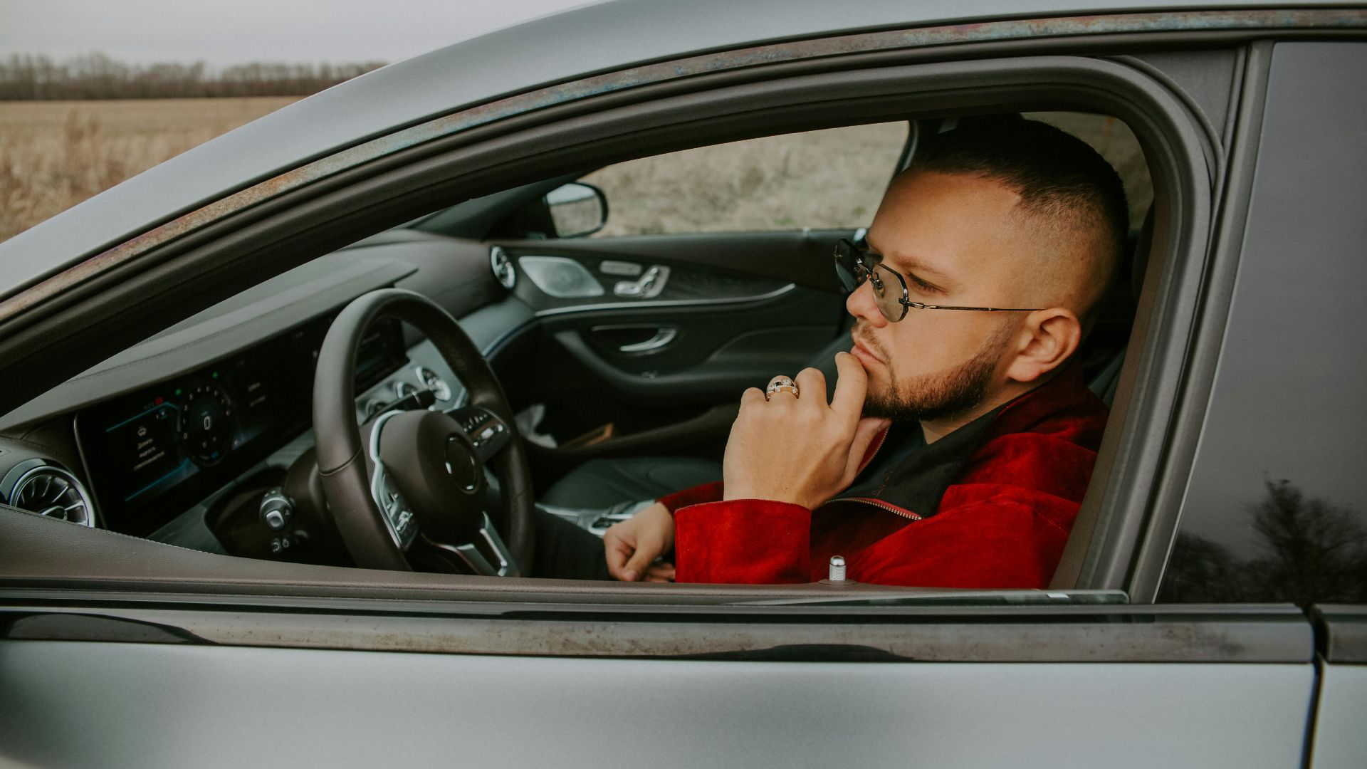 Side view of thoughtful young bearded male in eyeglasses sitting in driver seat of car