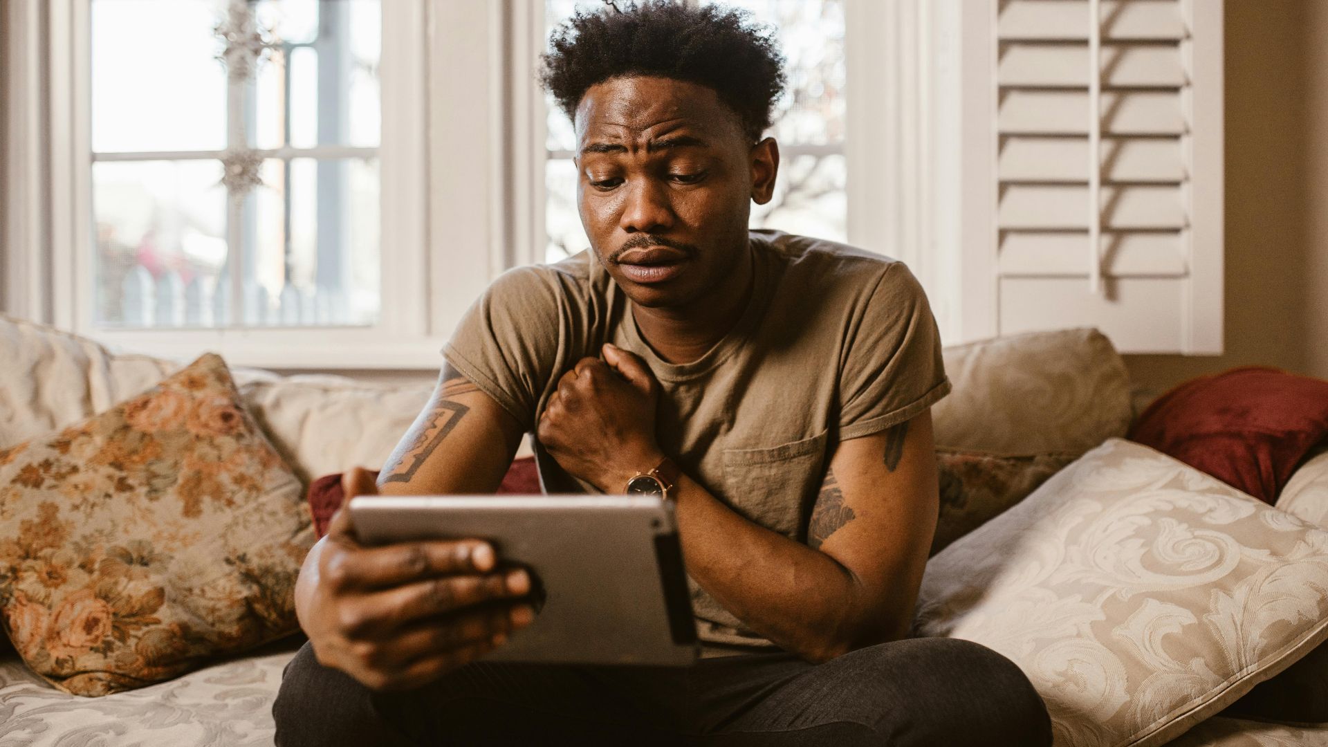 A man sitting on a sofa at home using a tablet with an emotional expression.