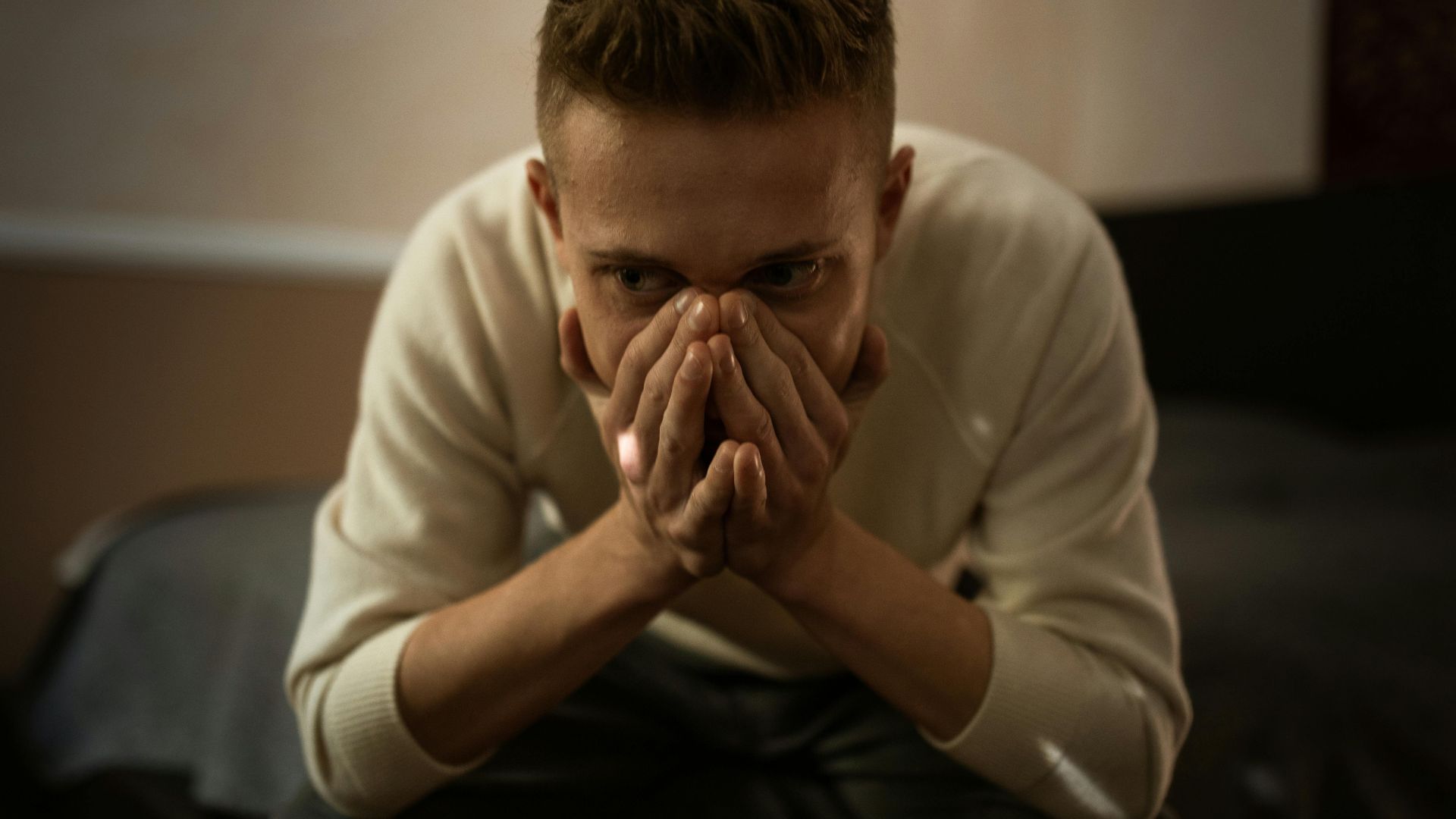 A worried man indoors covering his face with hands, depicting stress or contemplation.