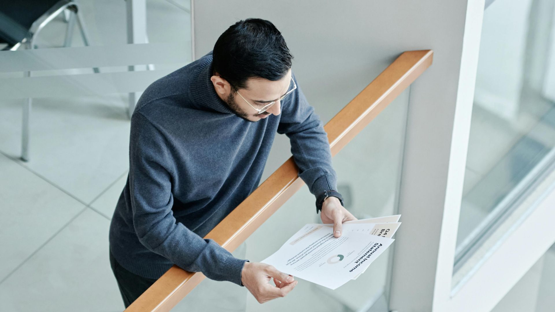A professional man examines papers in a bright, contemporary office space with glass walls.