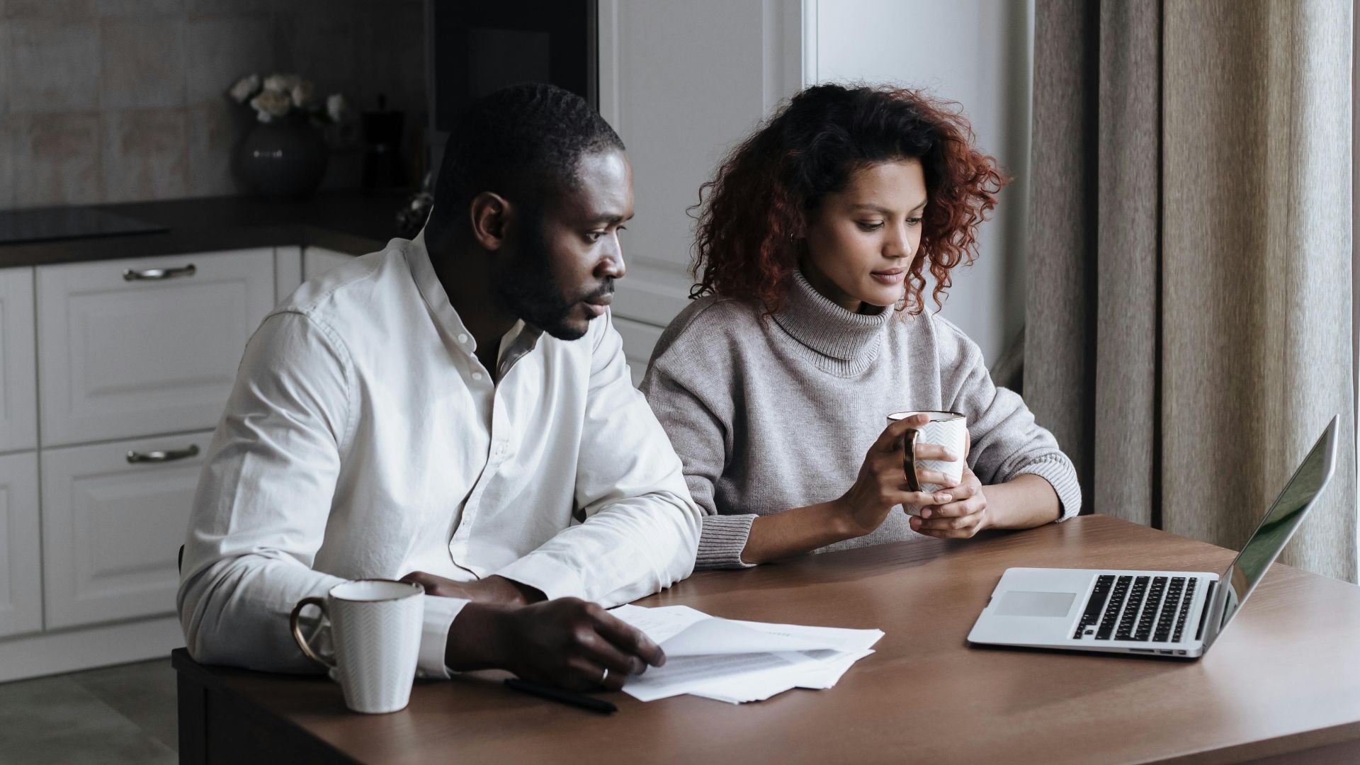 A couple working together on a laptop in their cozy kitchen, morning light.