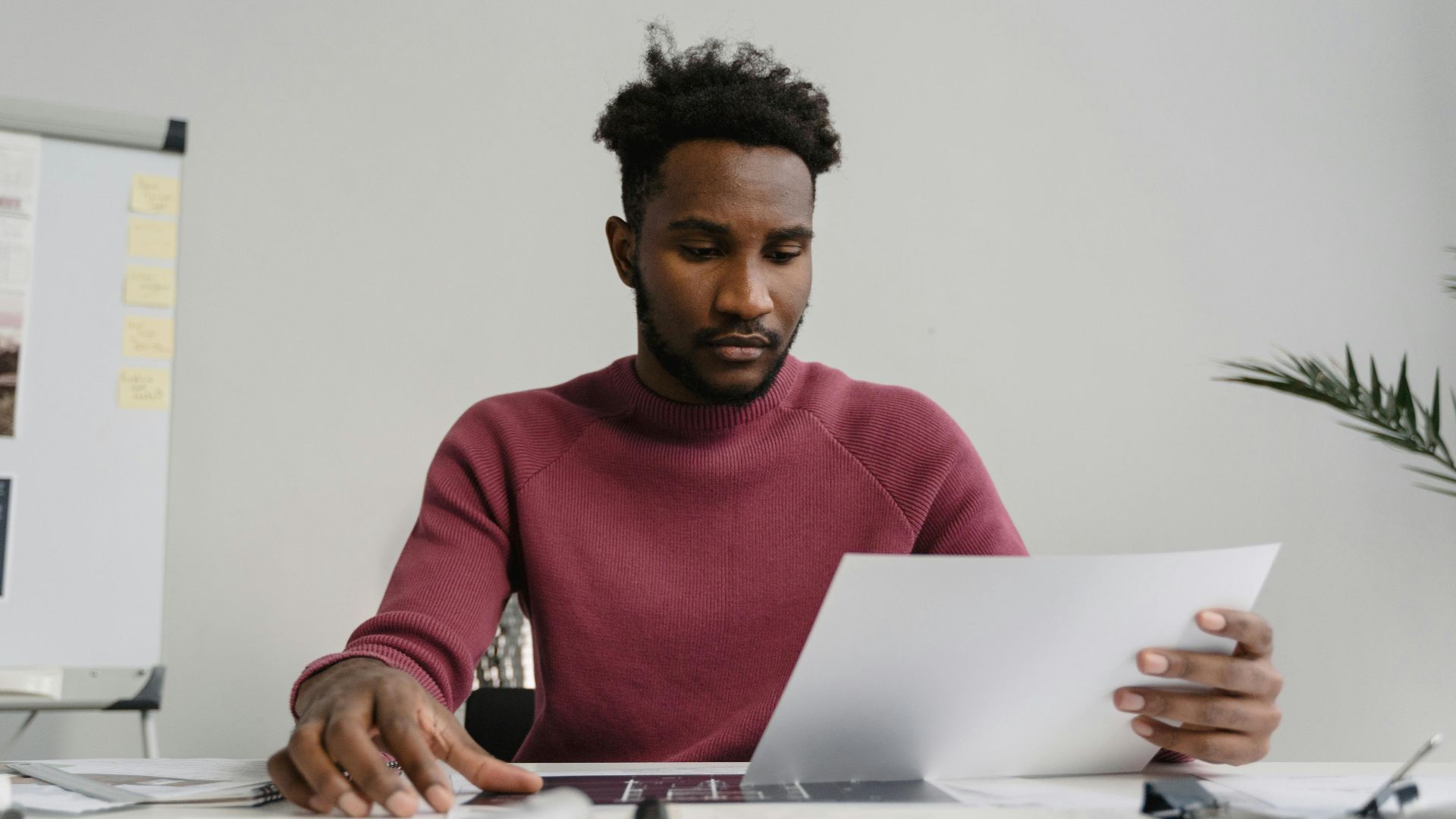 A man in a workspace analyzing a white document attentively. Modern office environment.
