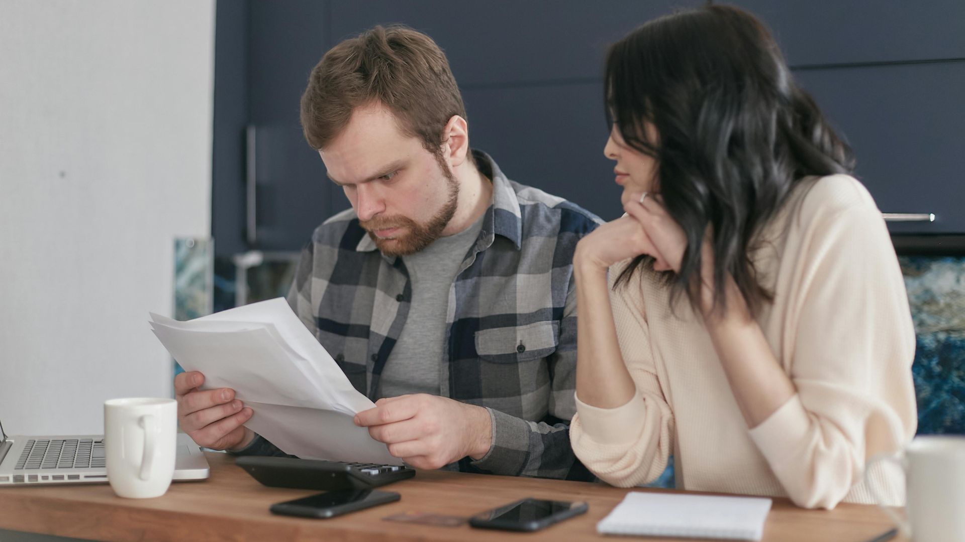 A focused couple sitting at a desk reviewing important documents in a home office setting.
