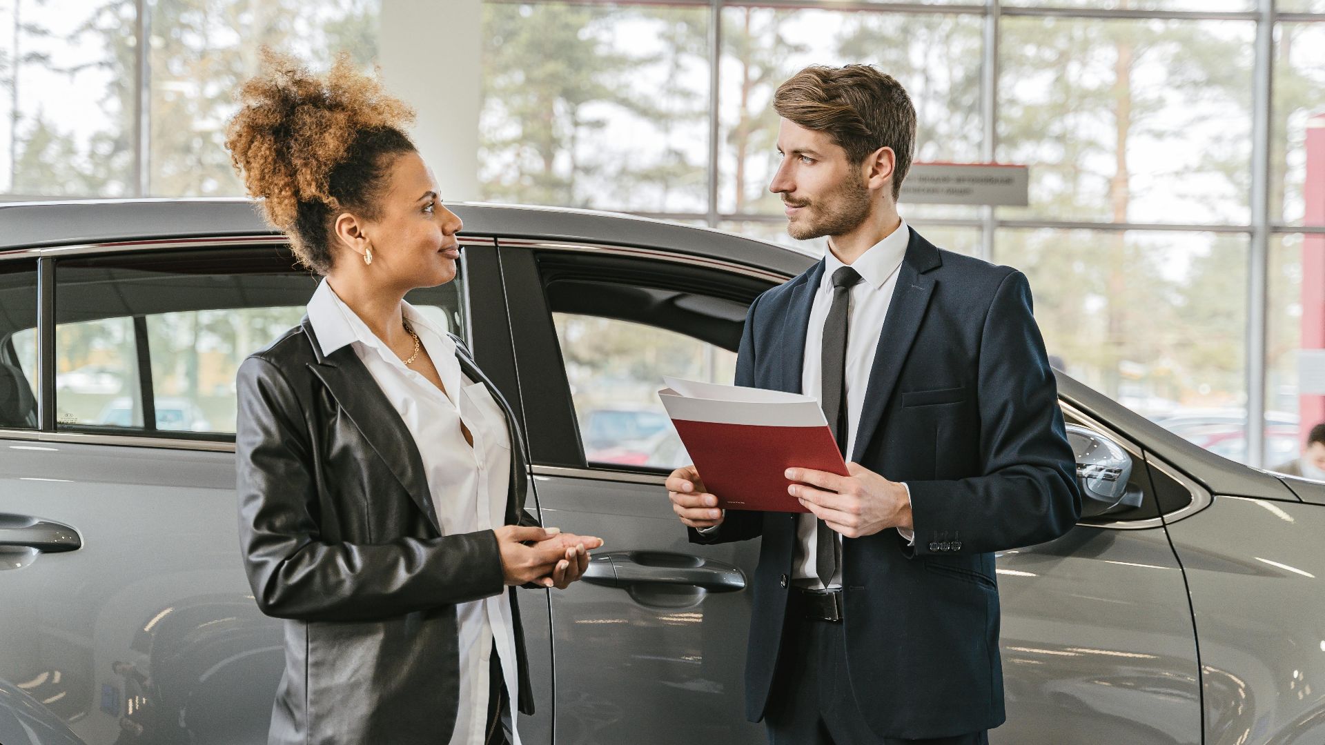 A woman discussing car purchase with a dealer inside a car dealership showroom.