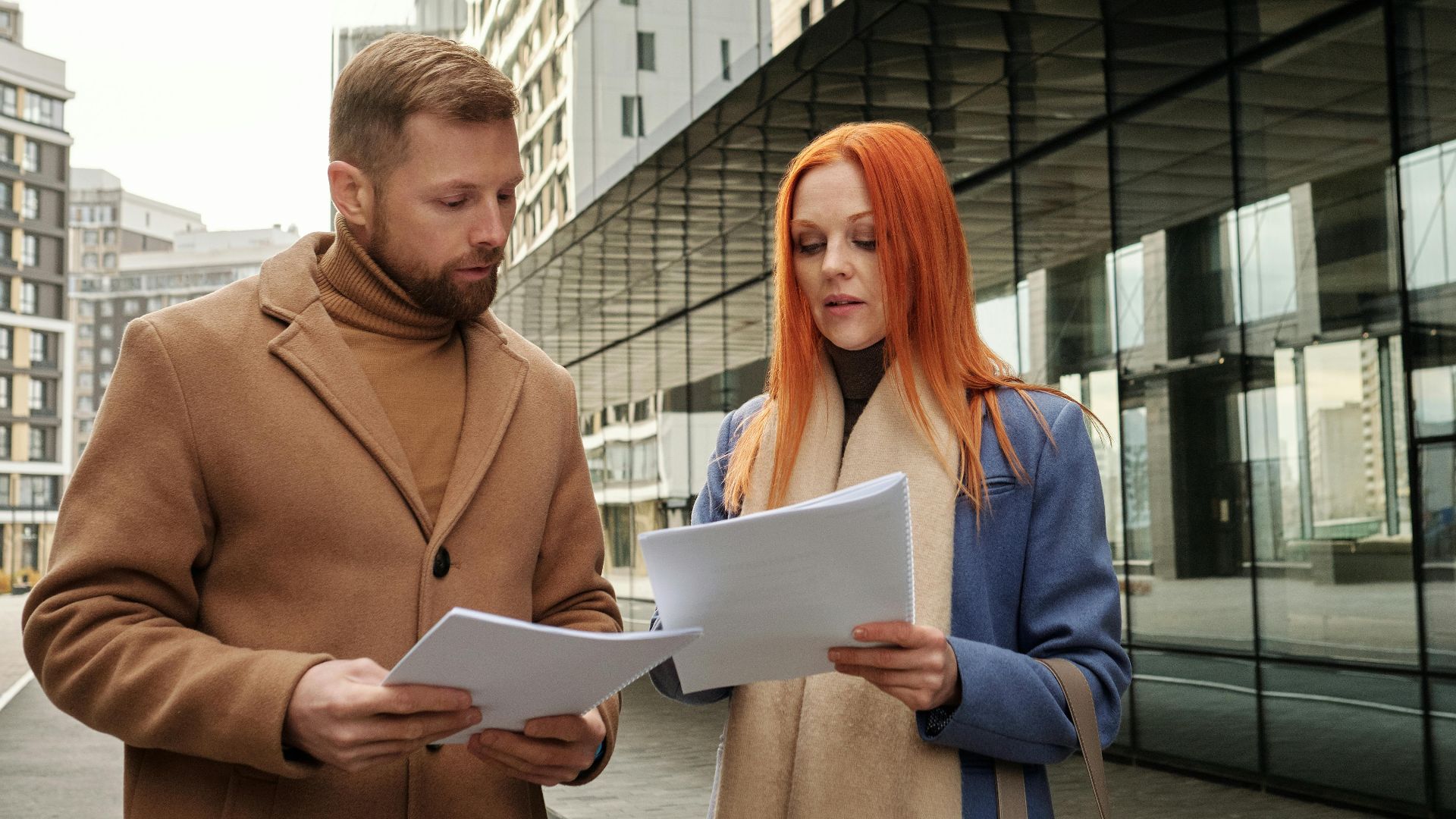 Two business professionals in urban setting reviewing documents together.