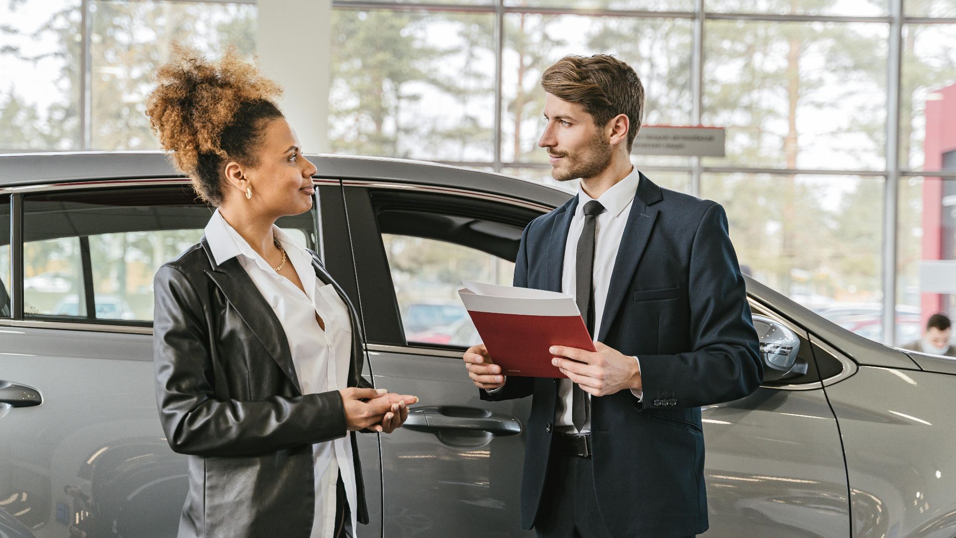 A woman discussing car purchase with a dealer inside a car dealership showroom.
