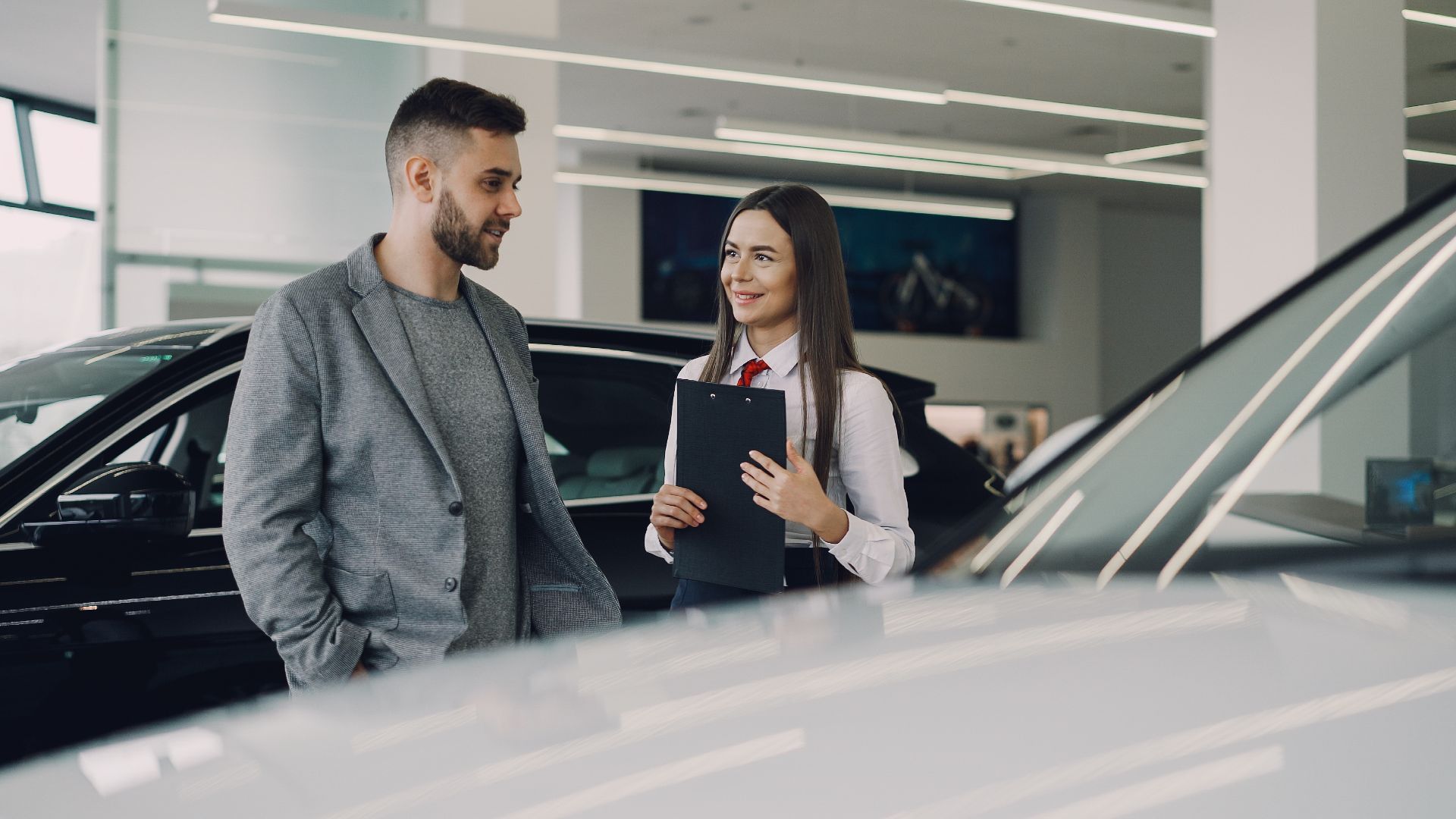 Man consults with salesperson in modern car dealership showroom.