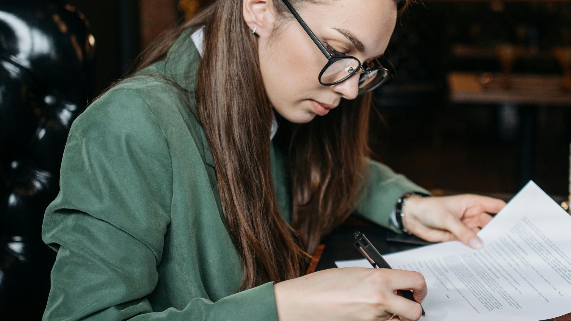 Focused businesswoman in green attire signing important documents at her desk.