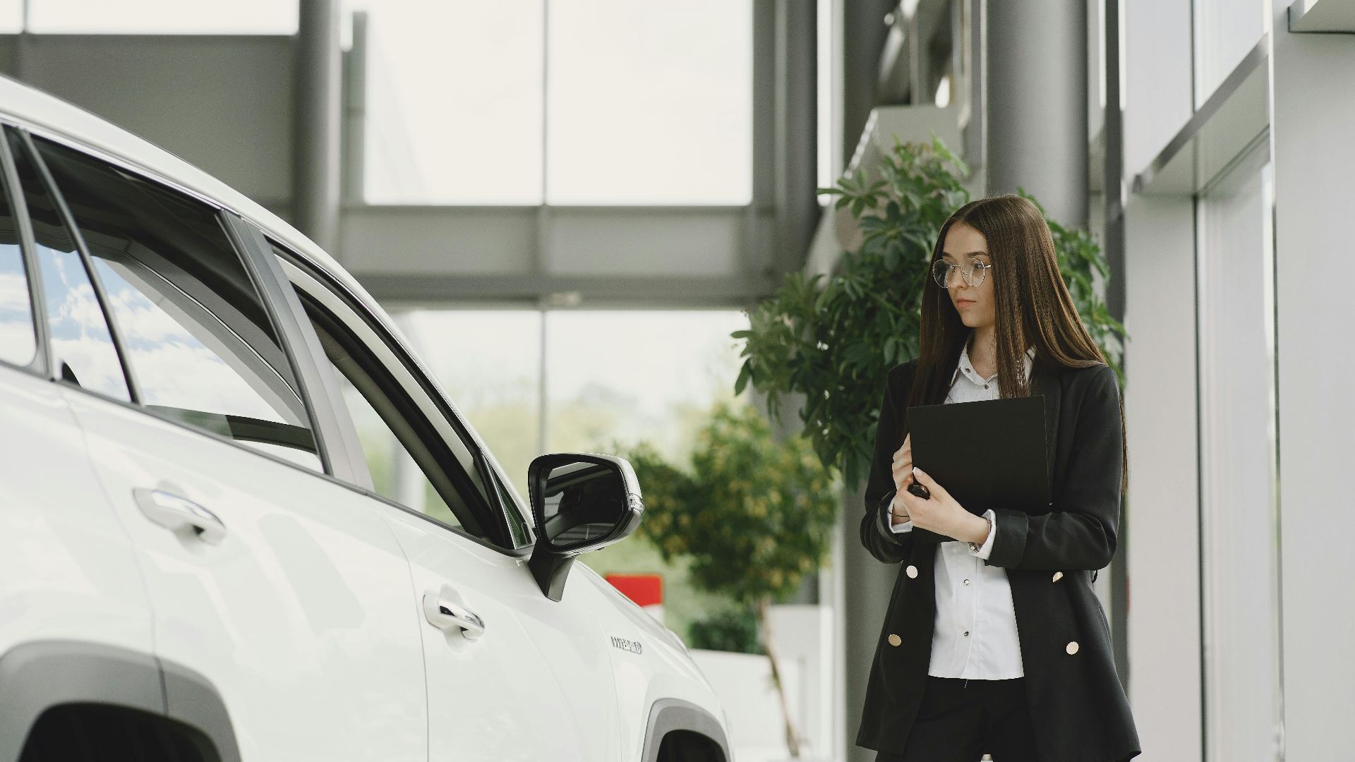 A businesswoman examines a luxurious vehicle inside a sleek, modern car dealership showroom.