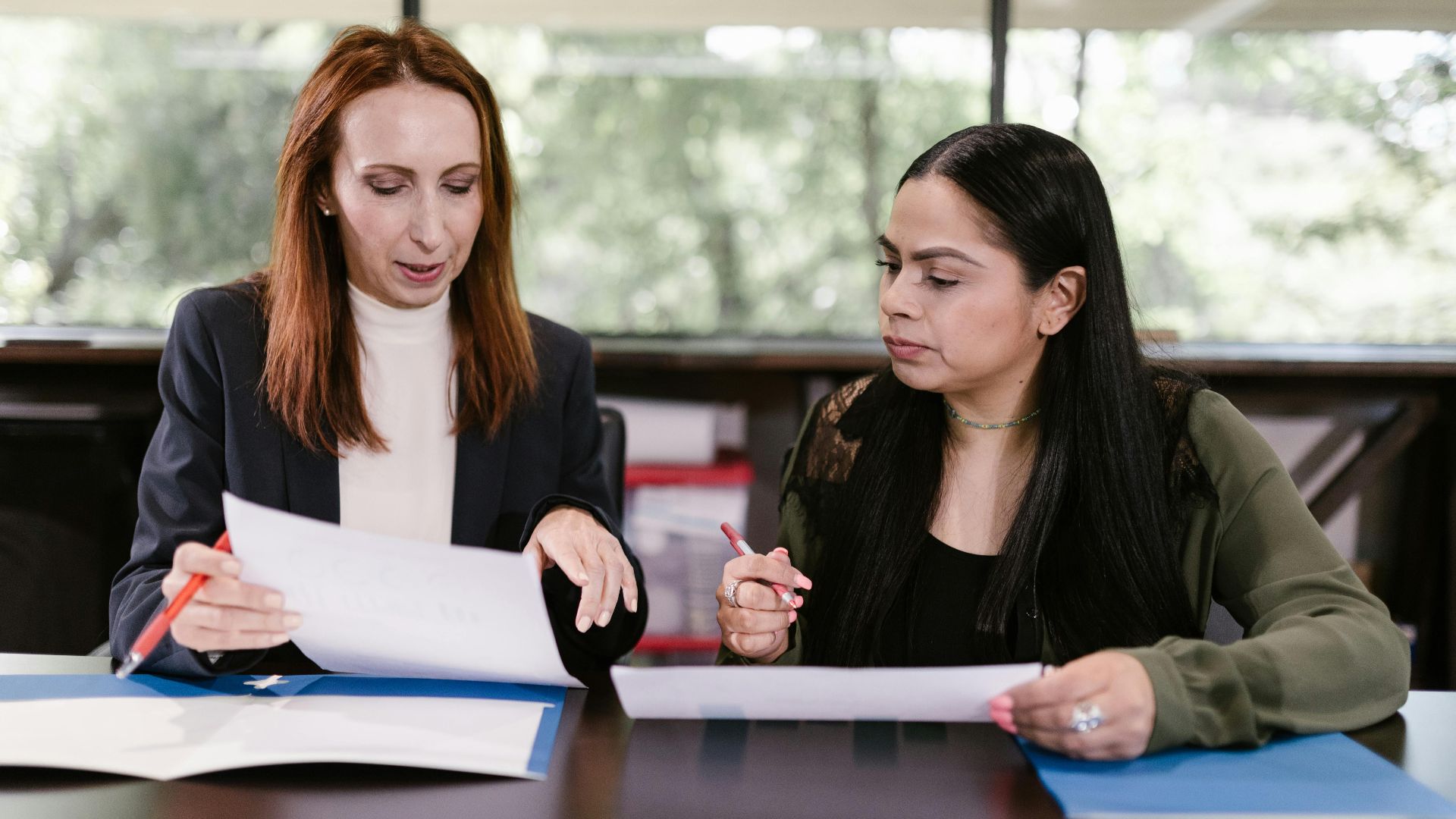 Two professional women reviewing documents in a well-lit office setting.