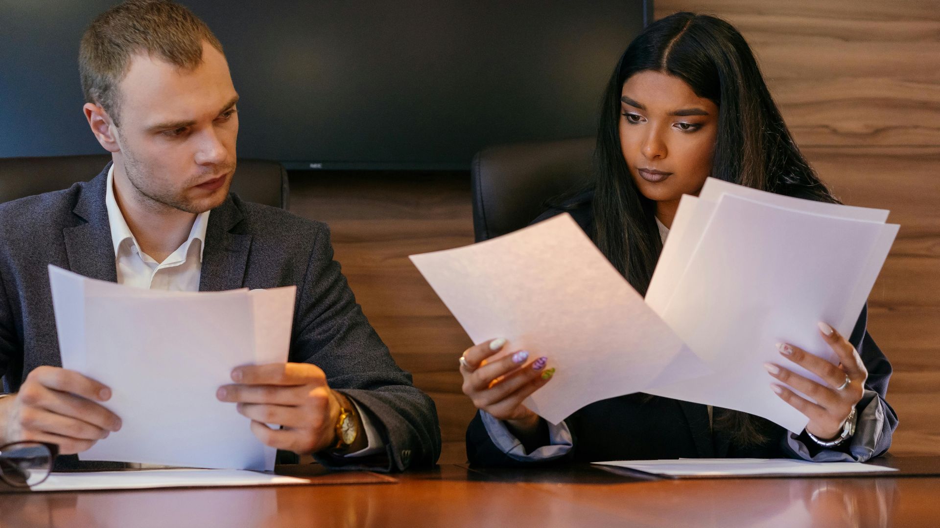 Two diverse professionals reviewing documents in a modern office setting, showcasing teamwork and focus.