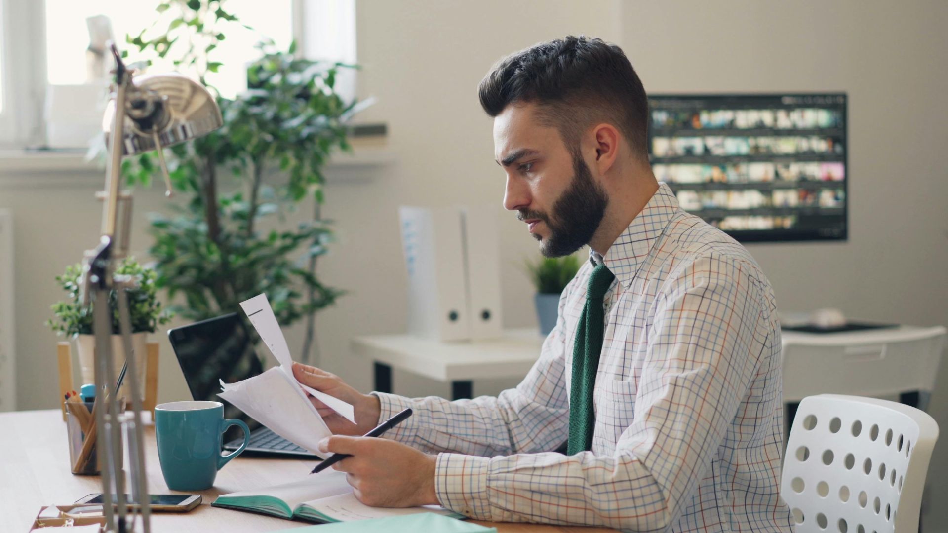 Focused man reviewing documents at a modern office desk with plants.