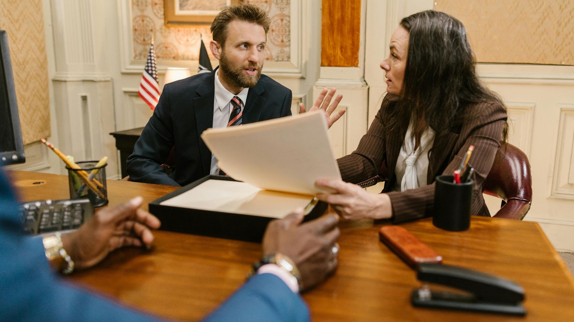 Diverse group in a corporate office engaged in a formal meeting. Professional attire and documents suggest a business discussion.