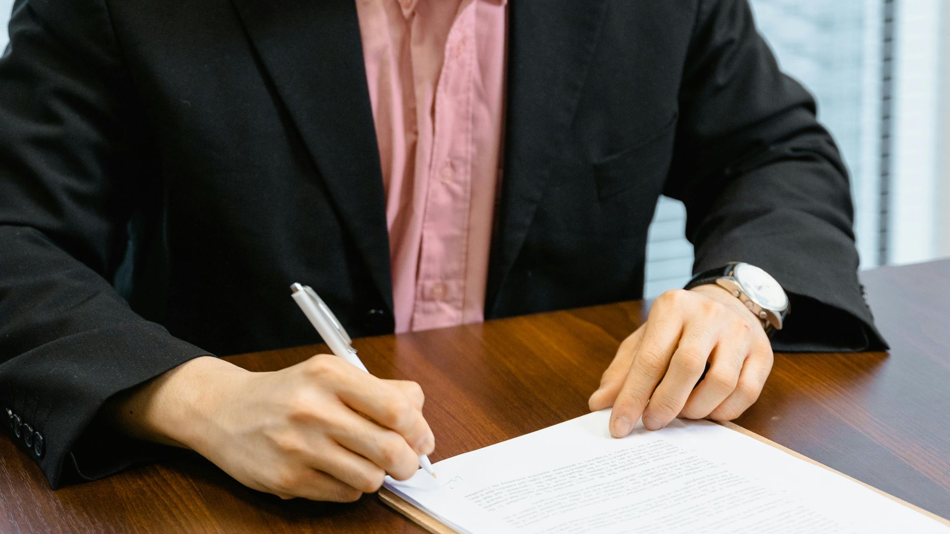Professional man in business attire signing papers at an office desk.