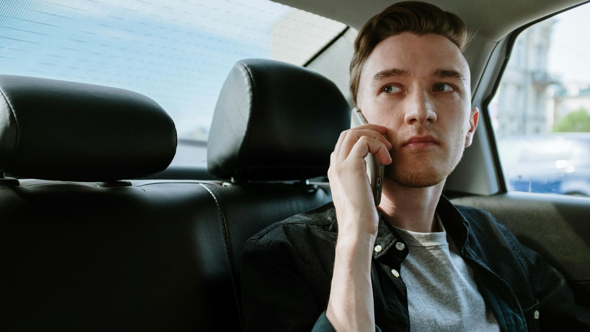 A young man talking on his phone while sitting in the backseat of a car.