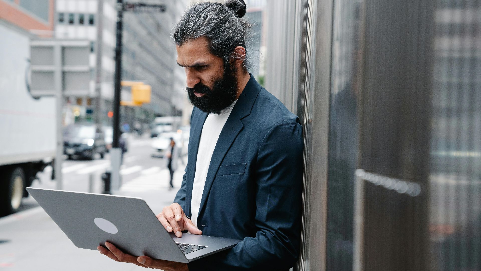 Bearded businessman focusing on laptop work in an urban outdoor setting.