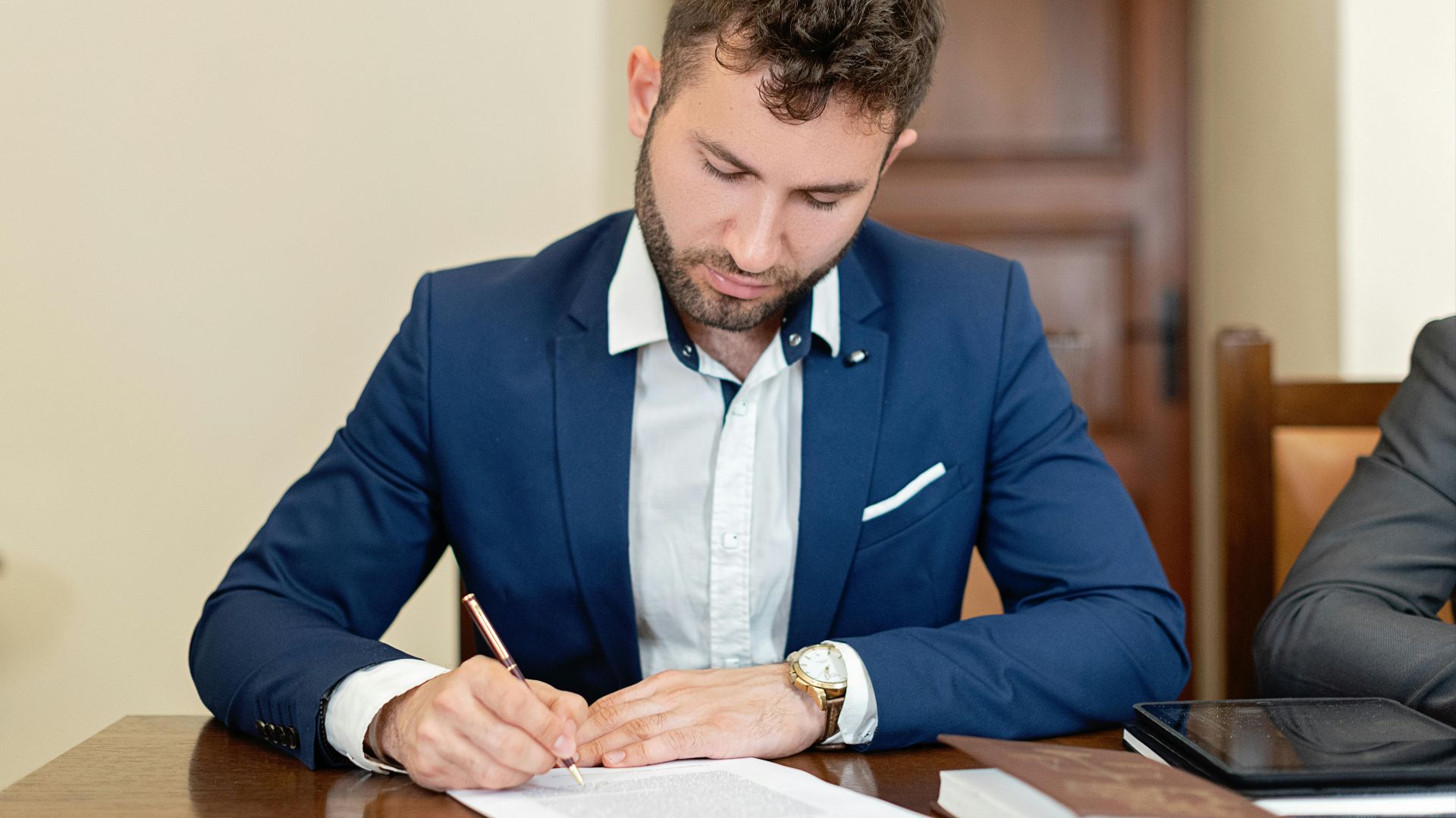 Confident businessman in a suit signing a contract at the office desk.