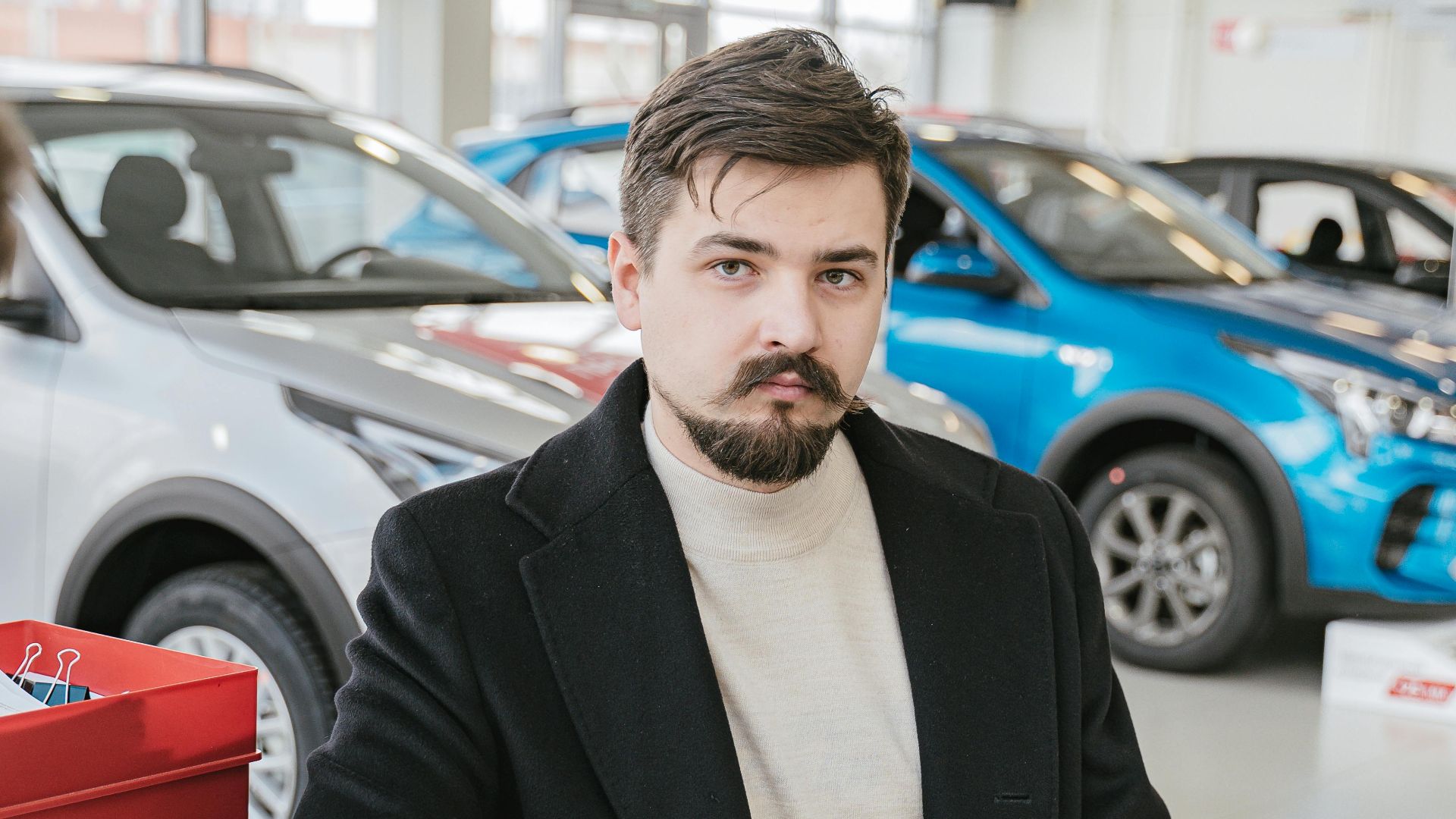 A man in a coat discusses with a sales representative in a bright, modern car showroom.