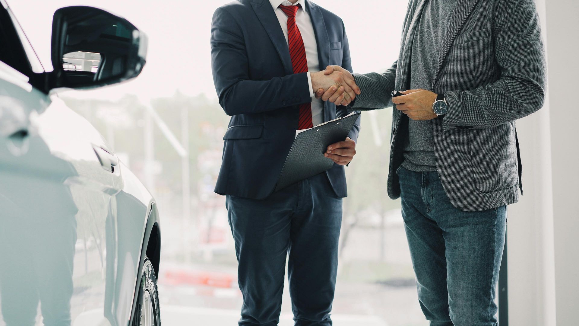 Two men shaking hands in a car dealership, symbolizing a successful business deal.