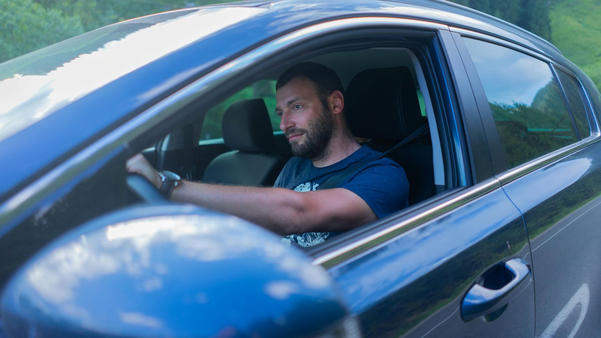 Bearded man enjoying a drive through lush green countryside on a sunny day.