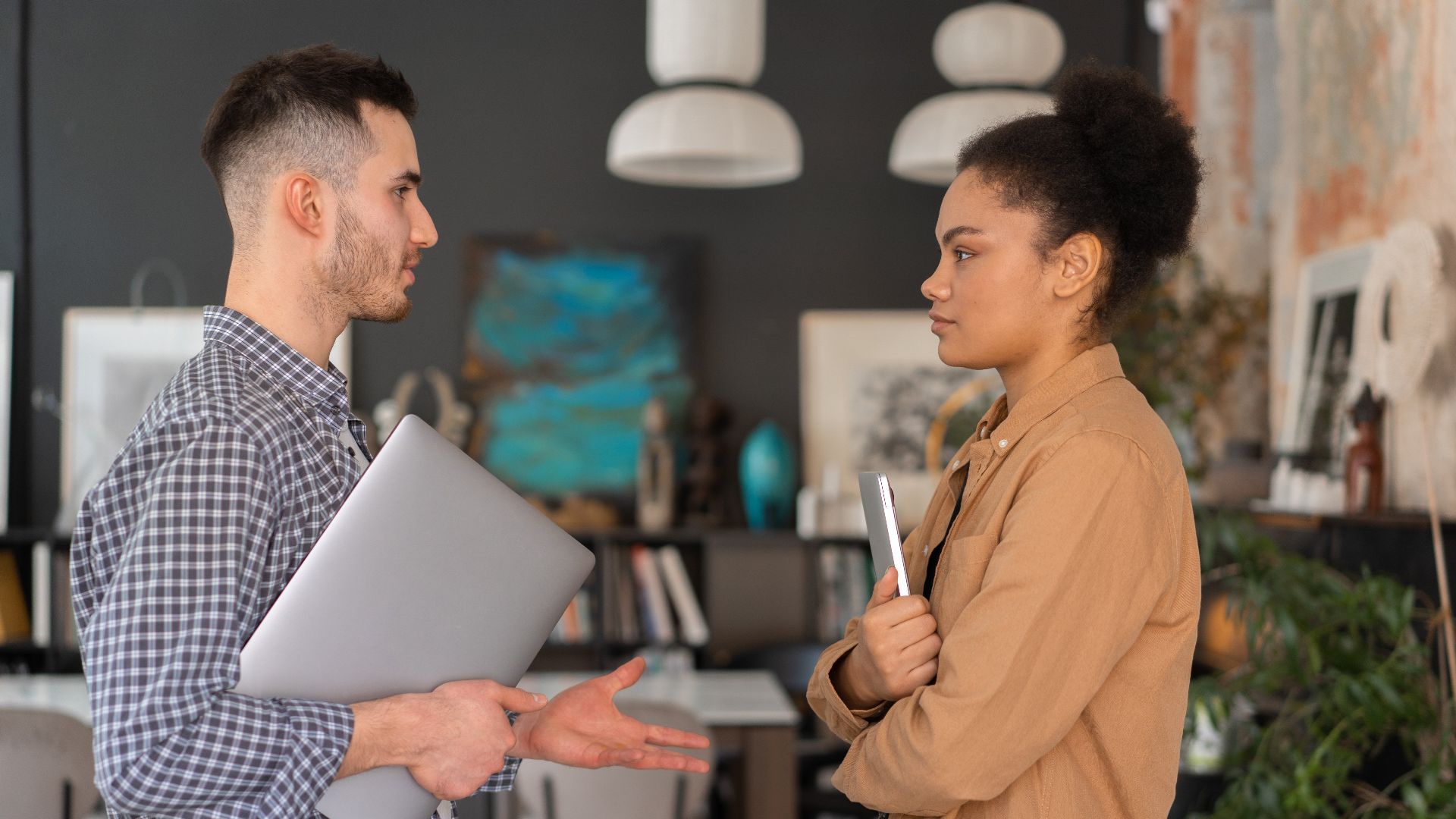 Two office workers engaged in a conversation, holding devices, in a modern office setting.