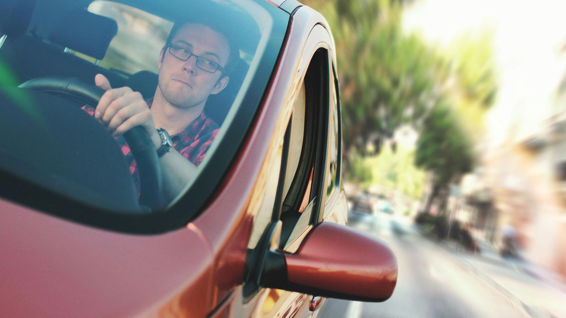 A man driving fast through a city street in a red car, showcasing motion and focus.