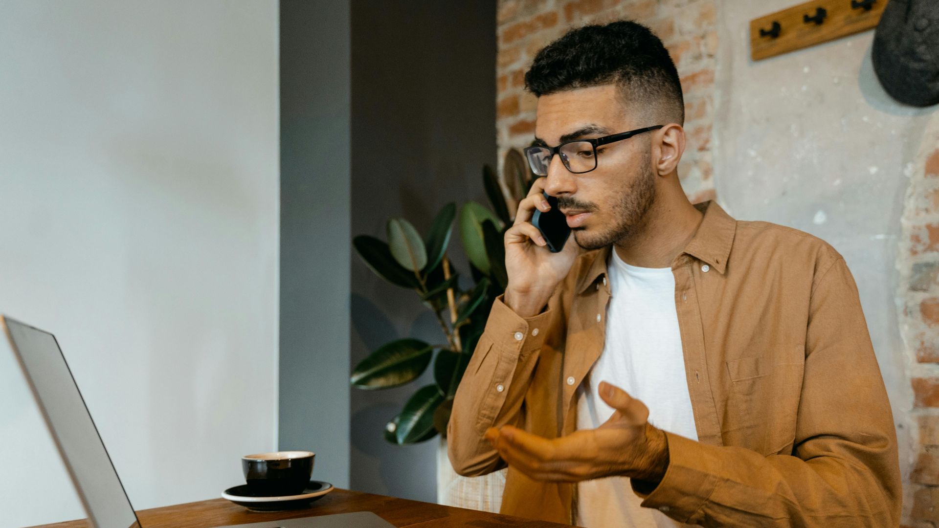 Man discussing on phone while working on laptop in a cozy home office setting.