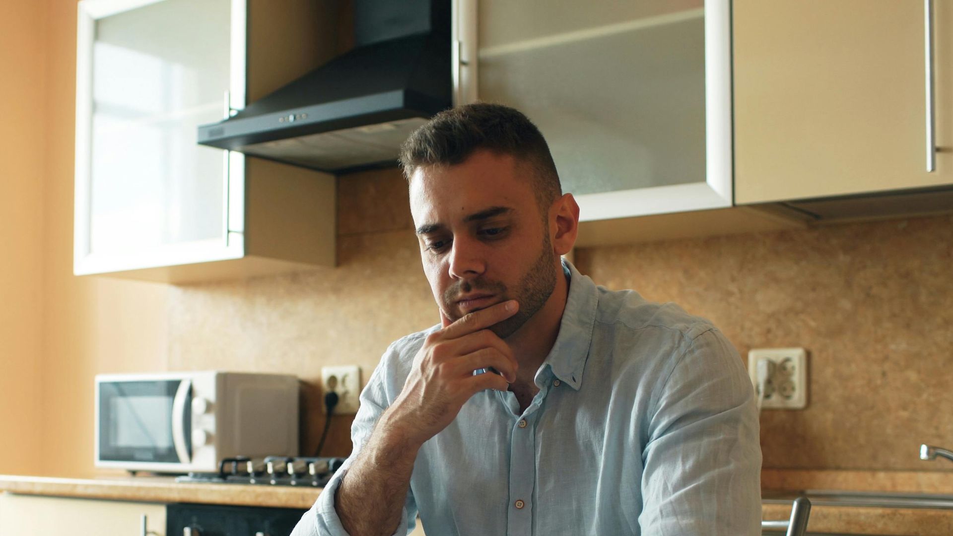 Thoughtful man reads a letter in a cozy kitchen setting with sunlight.