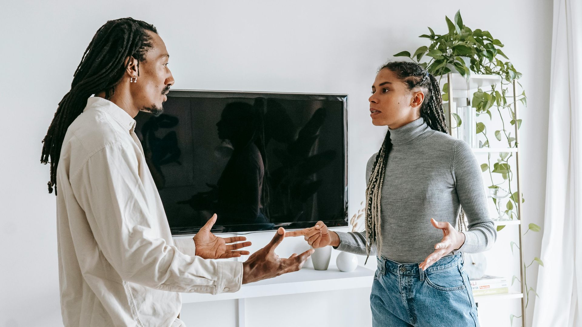 Side view of nervous young African American man and woman with dreadlocks in casual clothes quarreling together in light living room