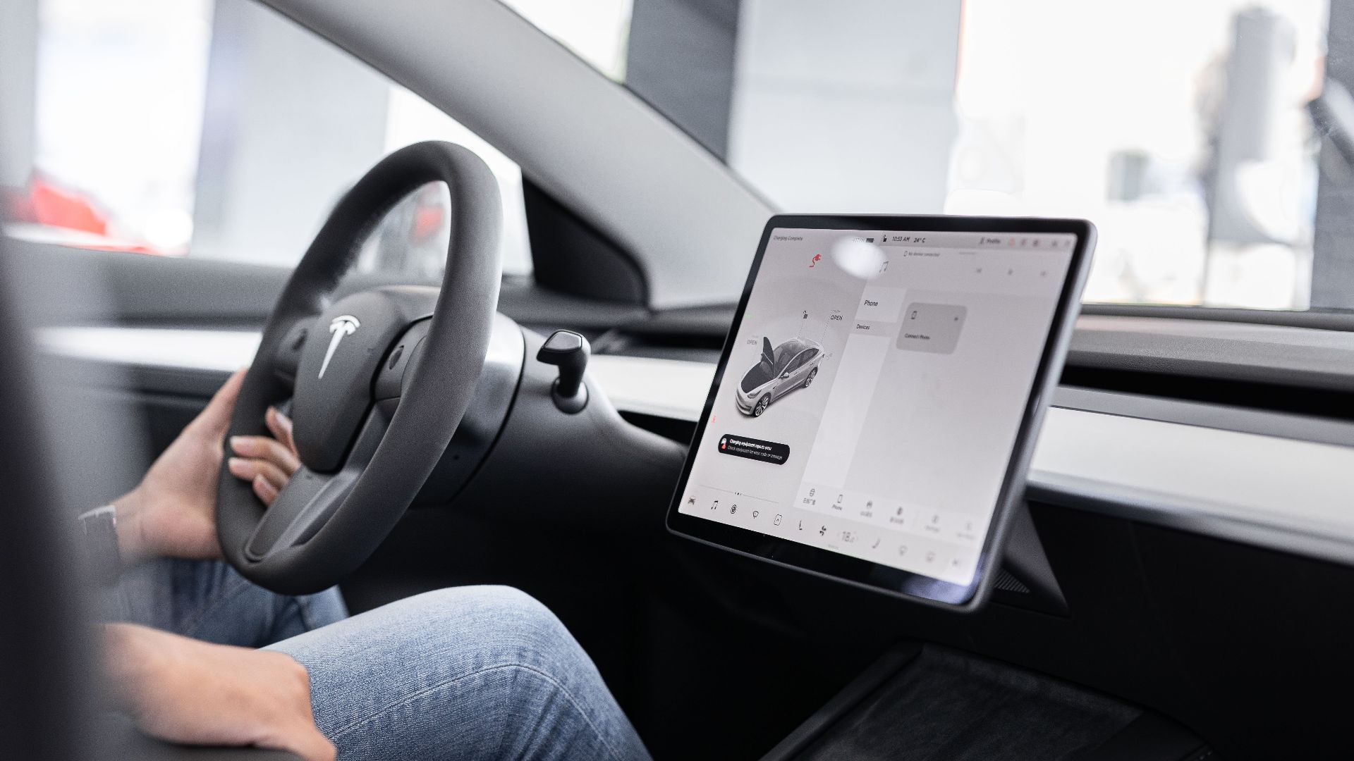 Interior of an electric car showing steering wheel and large touchscreen display, indicating modern technology.